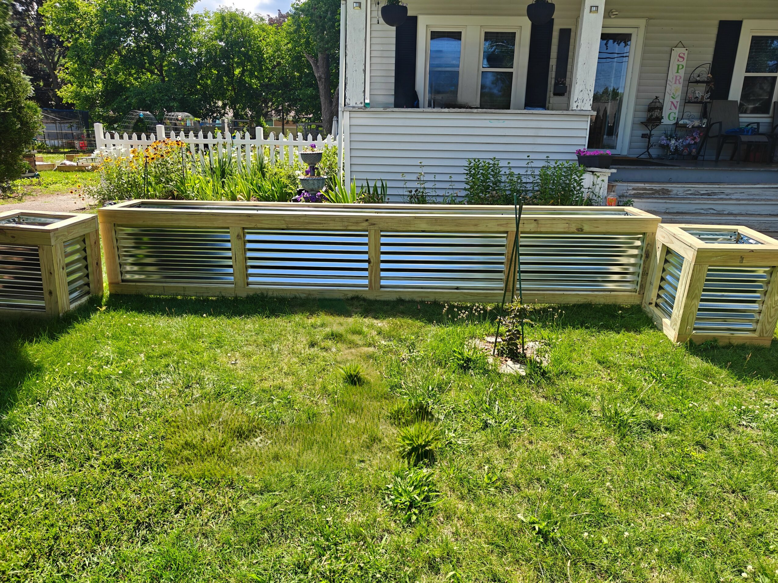 Front yard with a wooden fence, green grass, and a house in the background.