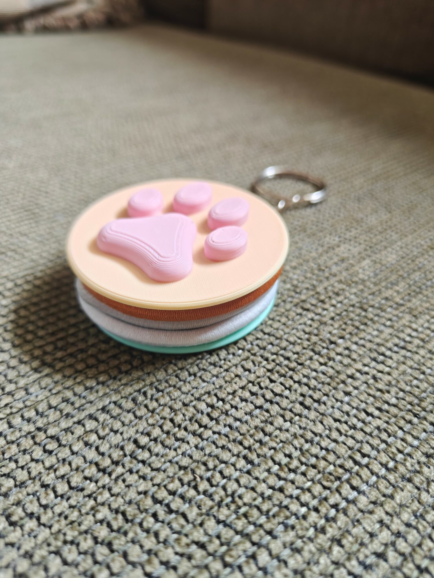 Small round keychain with pink and purple buttons on a textured gray surface.