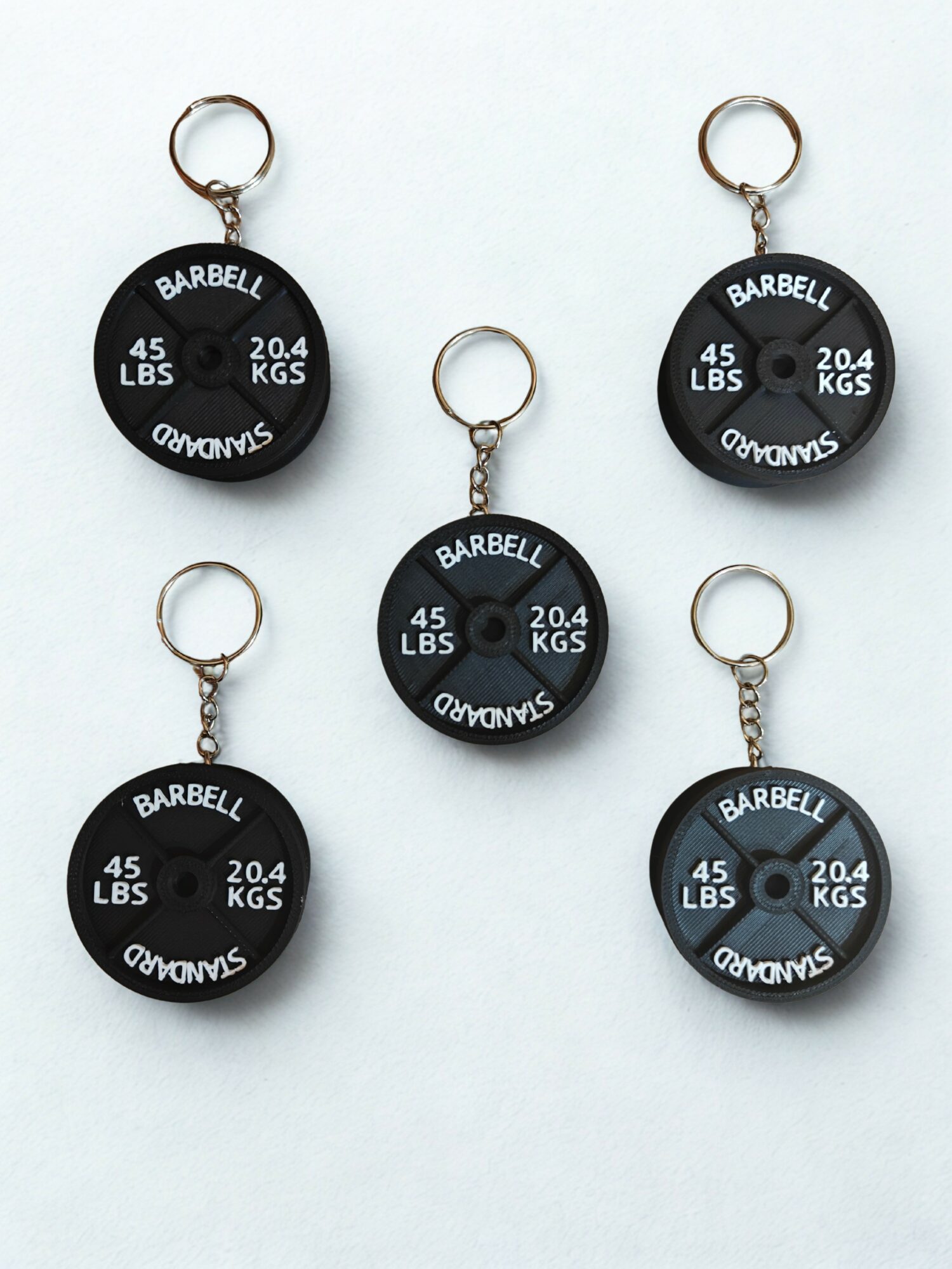 Six black circular keychains with weight and barbell information, arranged on a white background.
