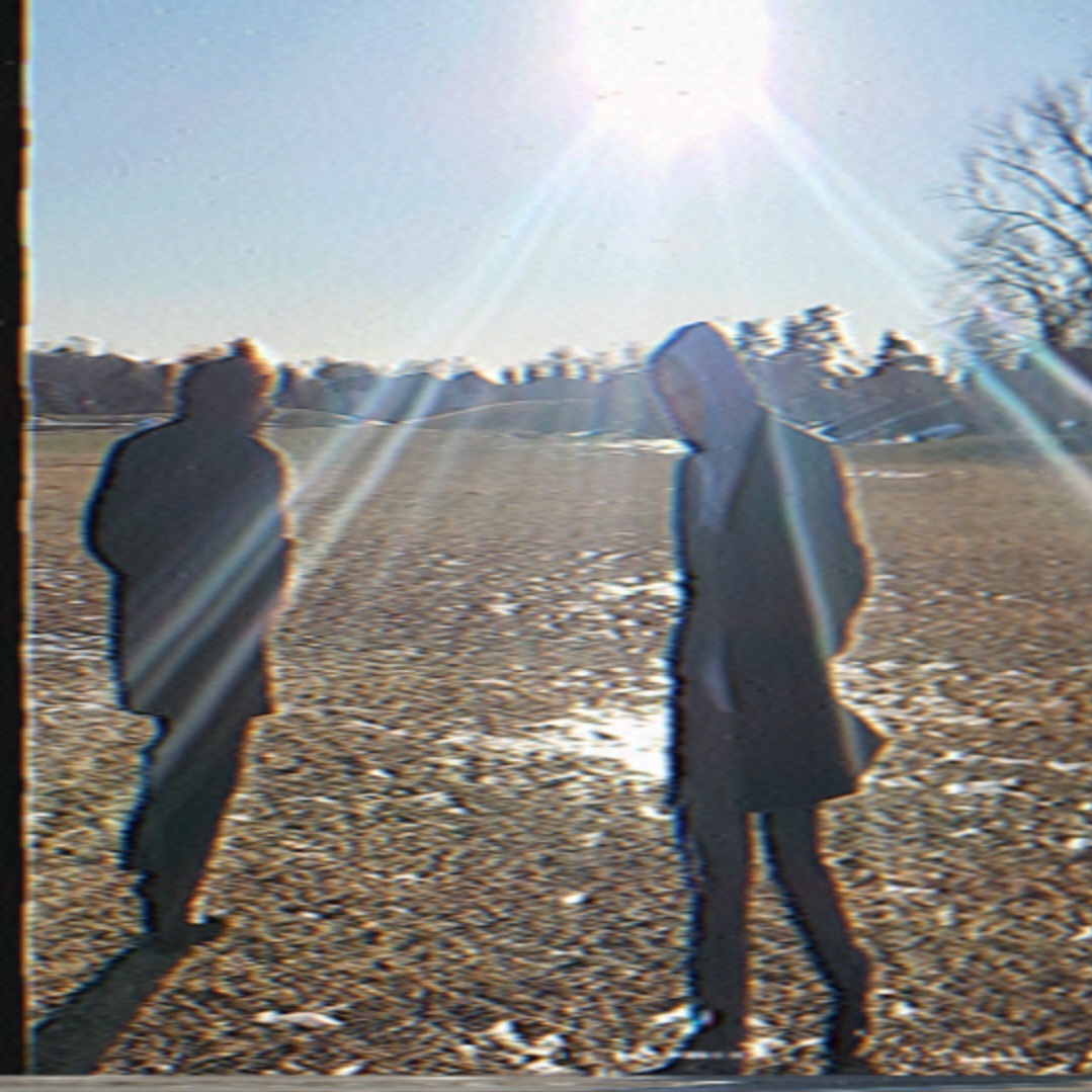 Two people walking on a field with the sun shining brightly overhead, creating lens flare effects.
