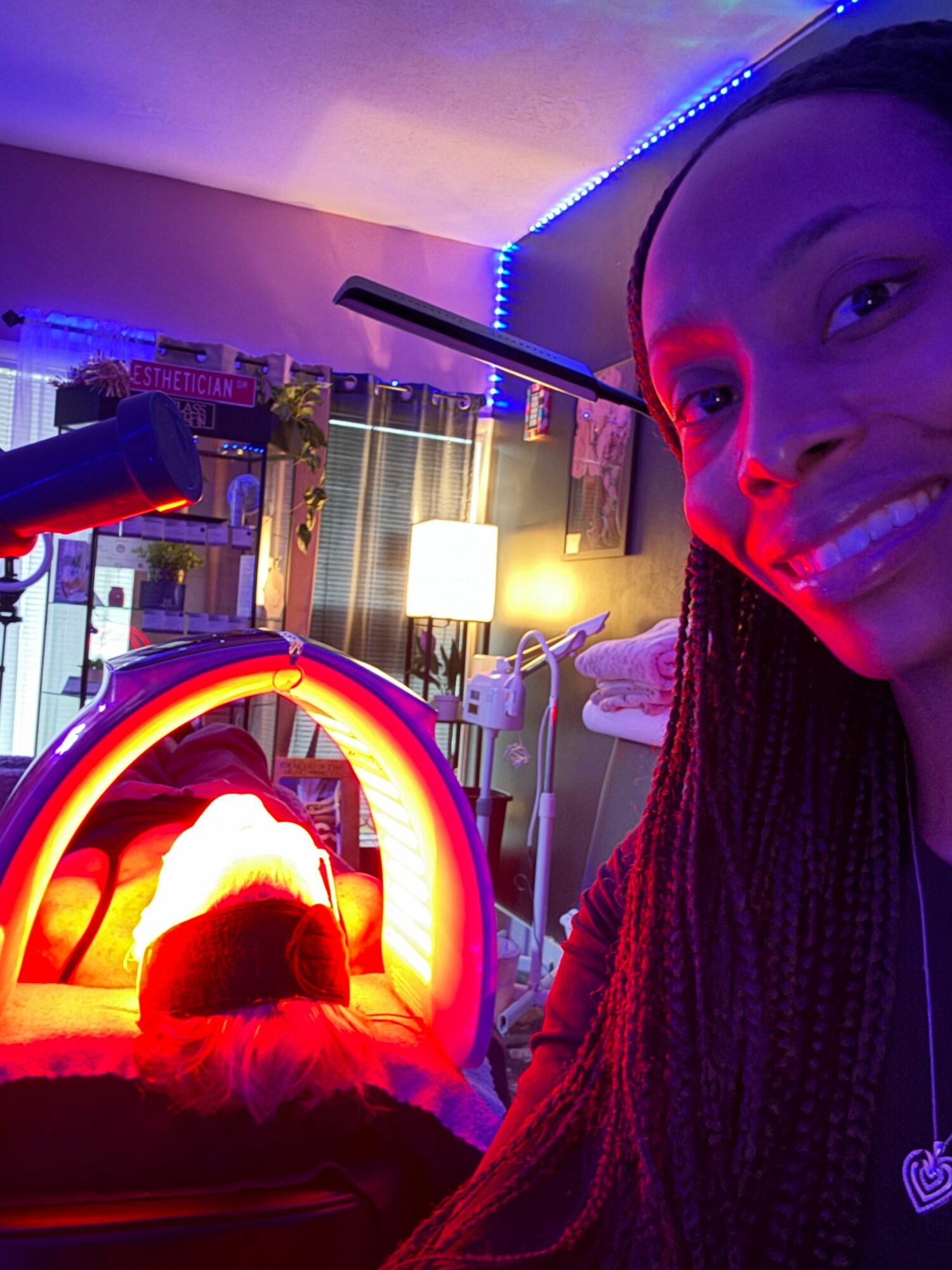 Person smiling with colorful lights and a glowing object in a room, illuminated by vibrant neon lighting.