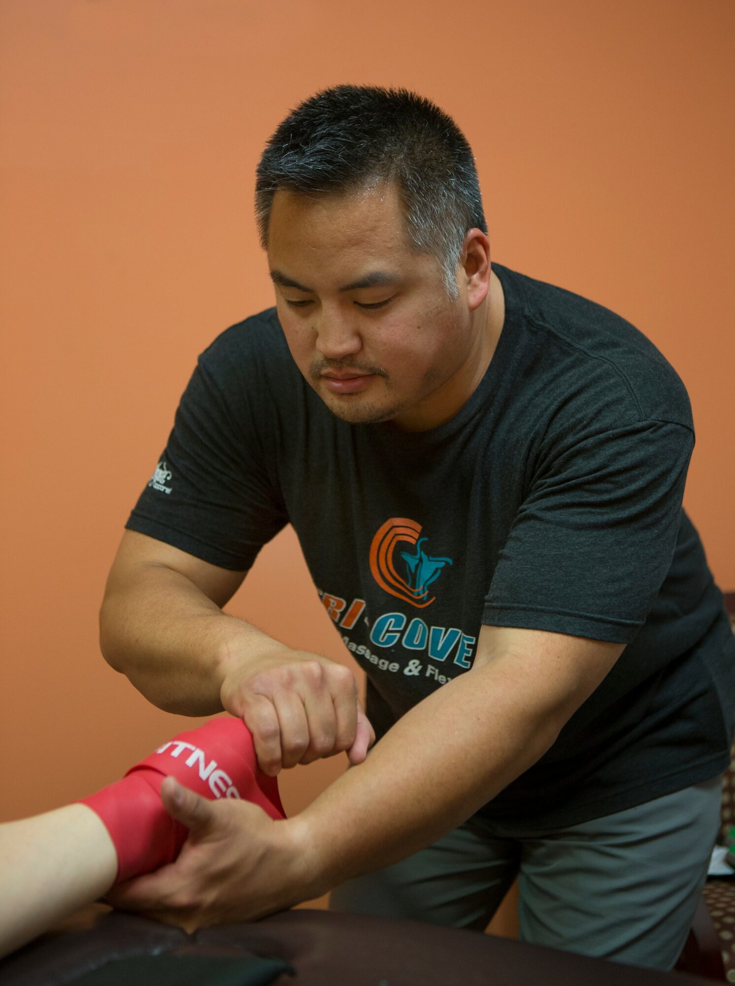 Man wrapping a person's wrist with a red bandage, focused on the task, against a plain orange background.