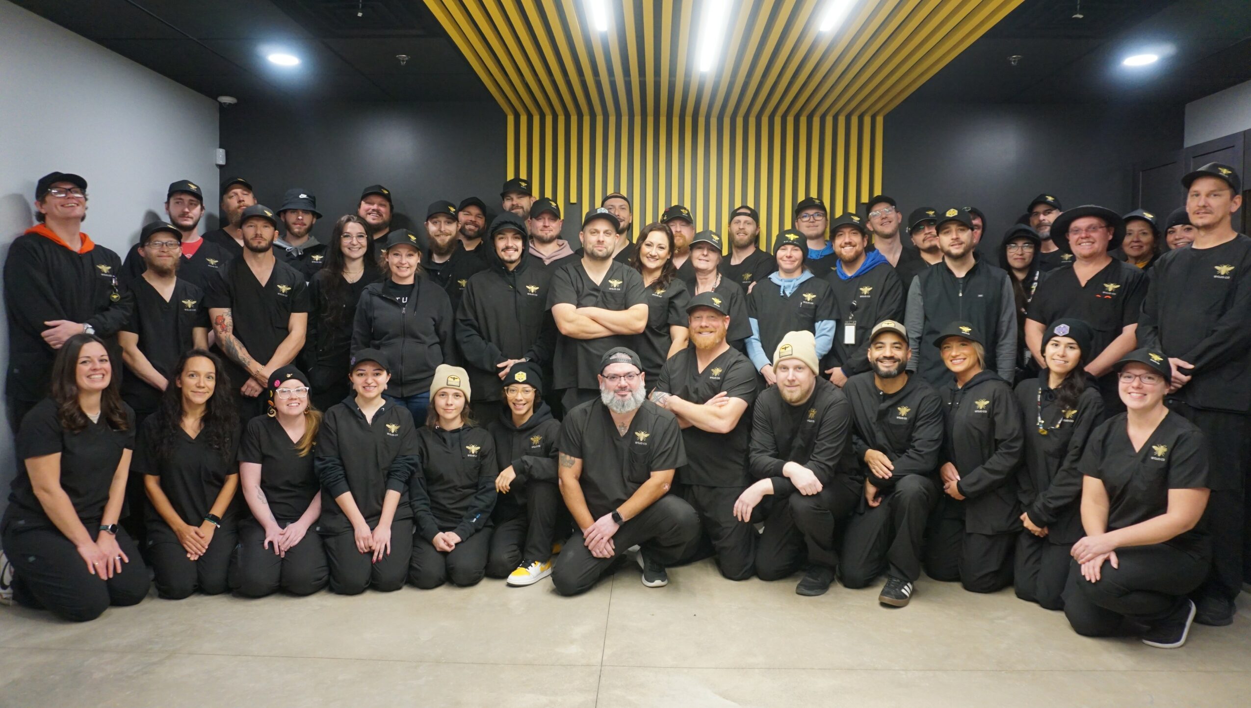 Group of people in black uniforms posing indoors with yellow and black decor in background.