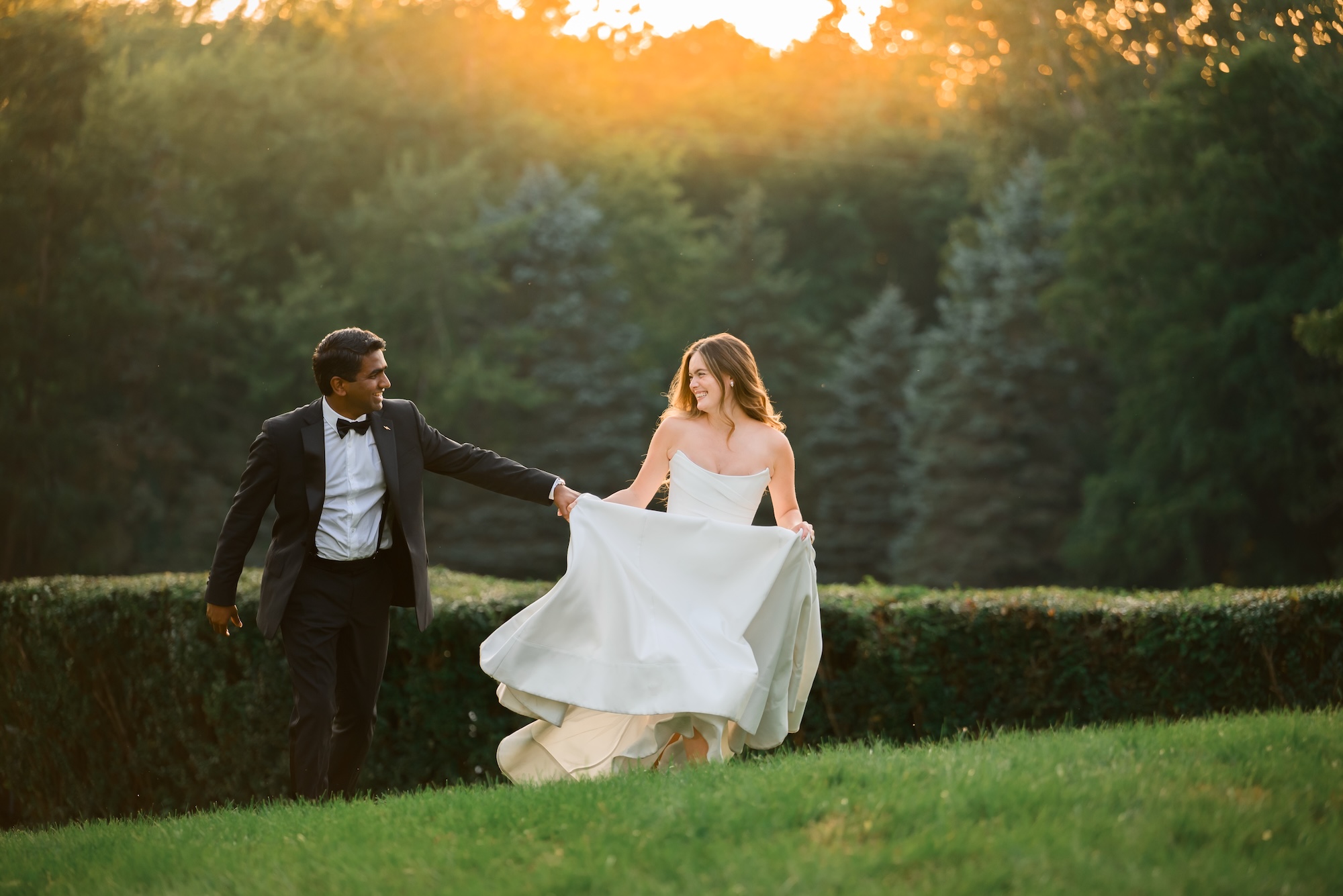 A couple holding hands outdoors during sunset, with trees in the background and a grassy foreground.