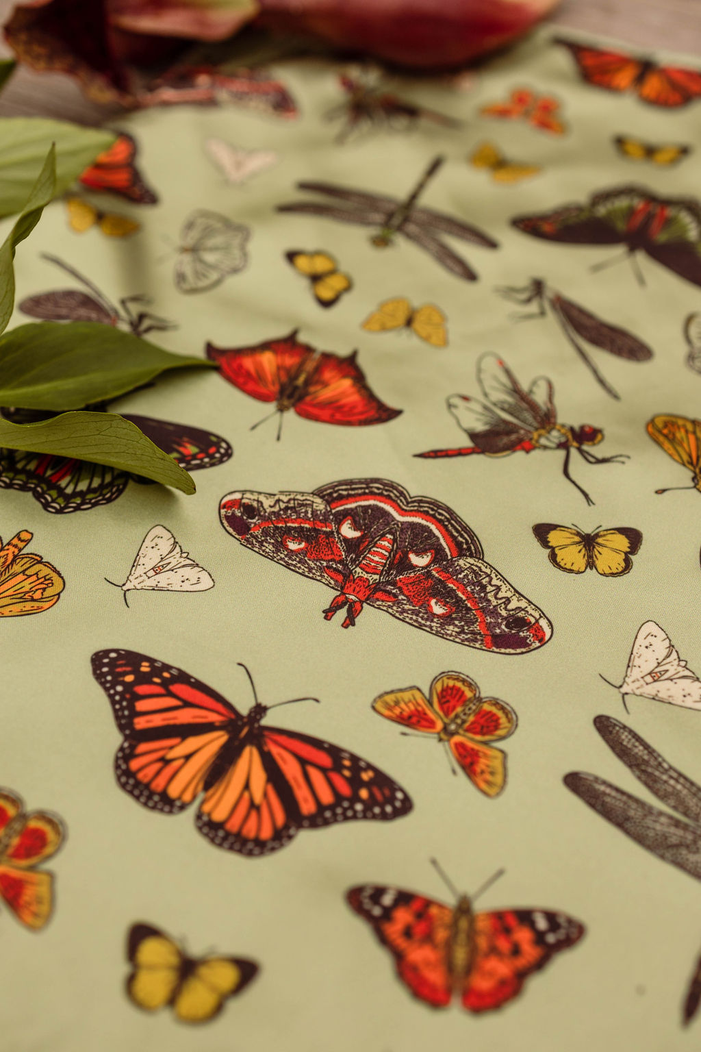 Fabric with colorful butterfly and dragonfly illustrations, some green leaves in the corner, on a light background.