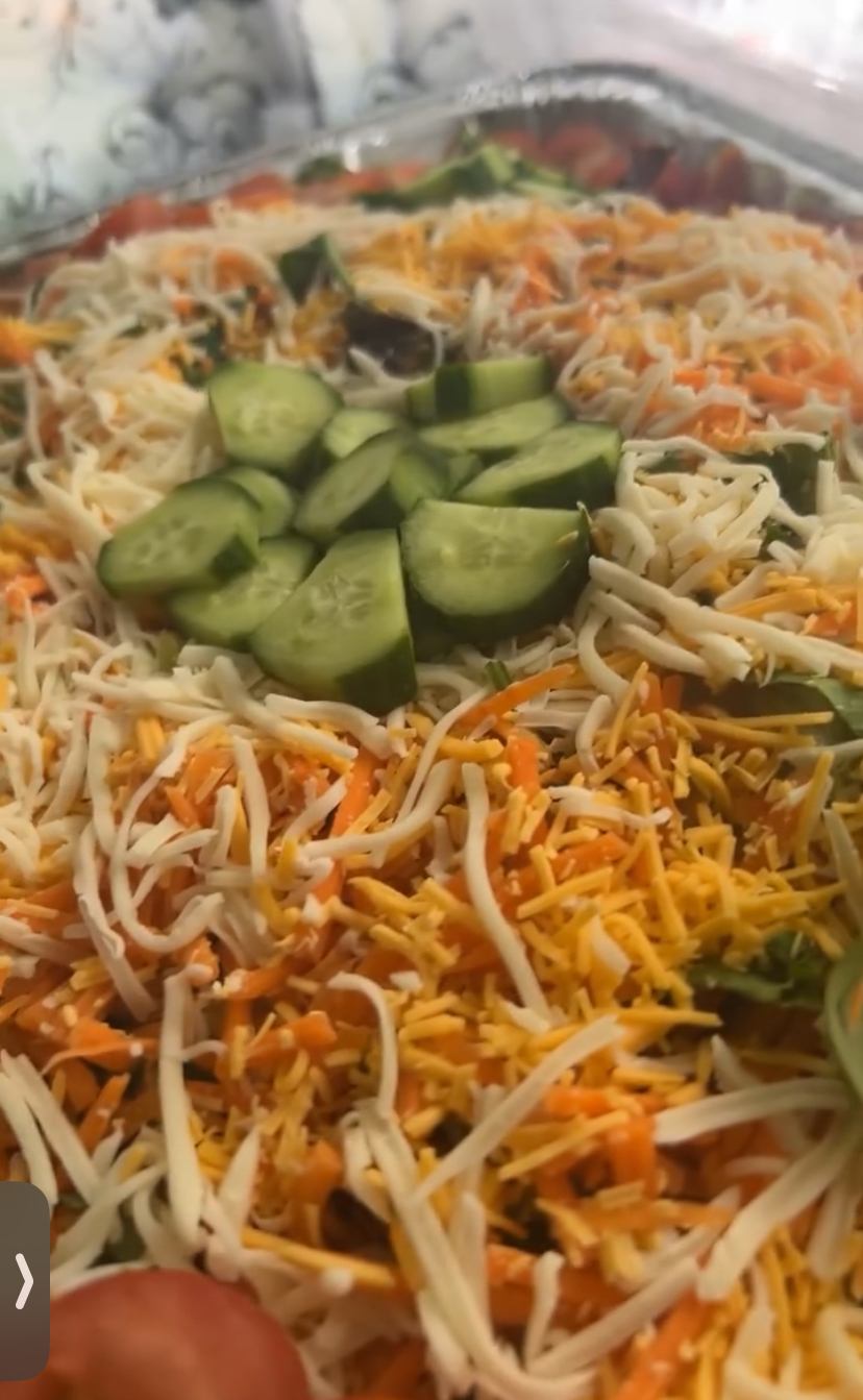 Close-up of a dish with shredded cheese, sliced cucumbers, and noodles with vegetables.
