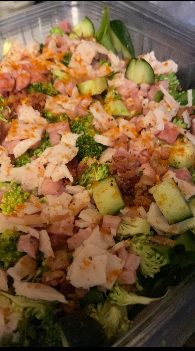 Mixed salad with chopped cucumbers, shredded chicken, and leafy greens in a container.