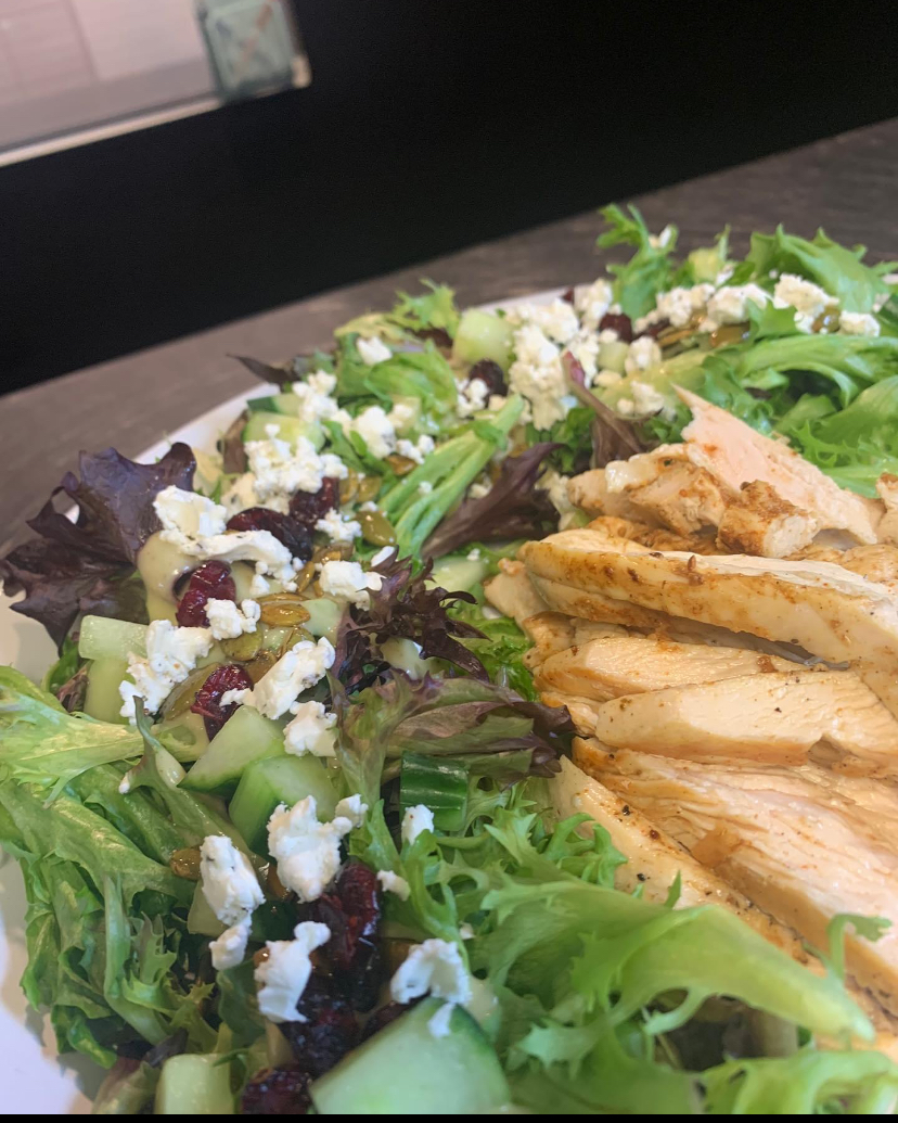Salad with mixed greens, cheese, and sliced grilled chicken on a plate.