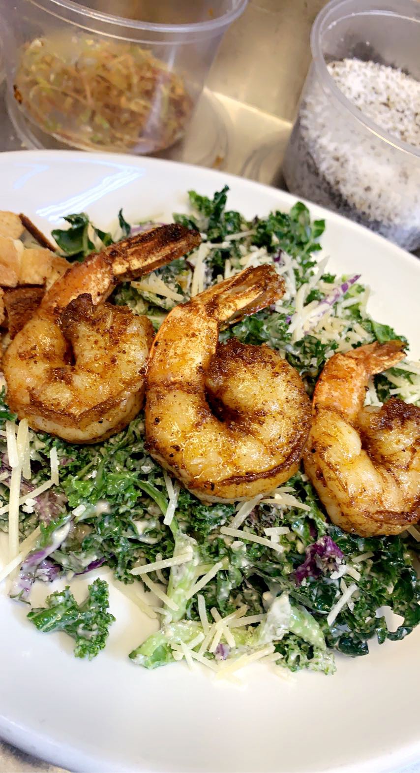 Plate with fried shrimp on leafy greens and shredded vegetables, with containers of noodles and powdered seasoning in the background.