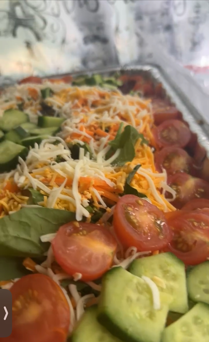 Salad with cherry tomatoes, cucumber, shredded cheese, and greens on a tray.