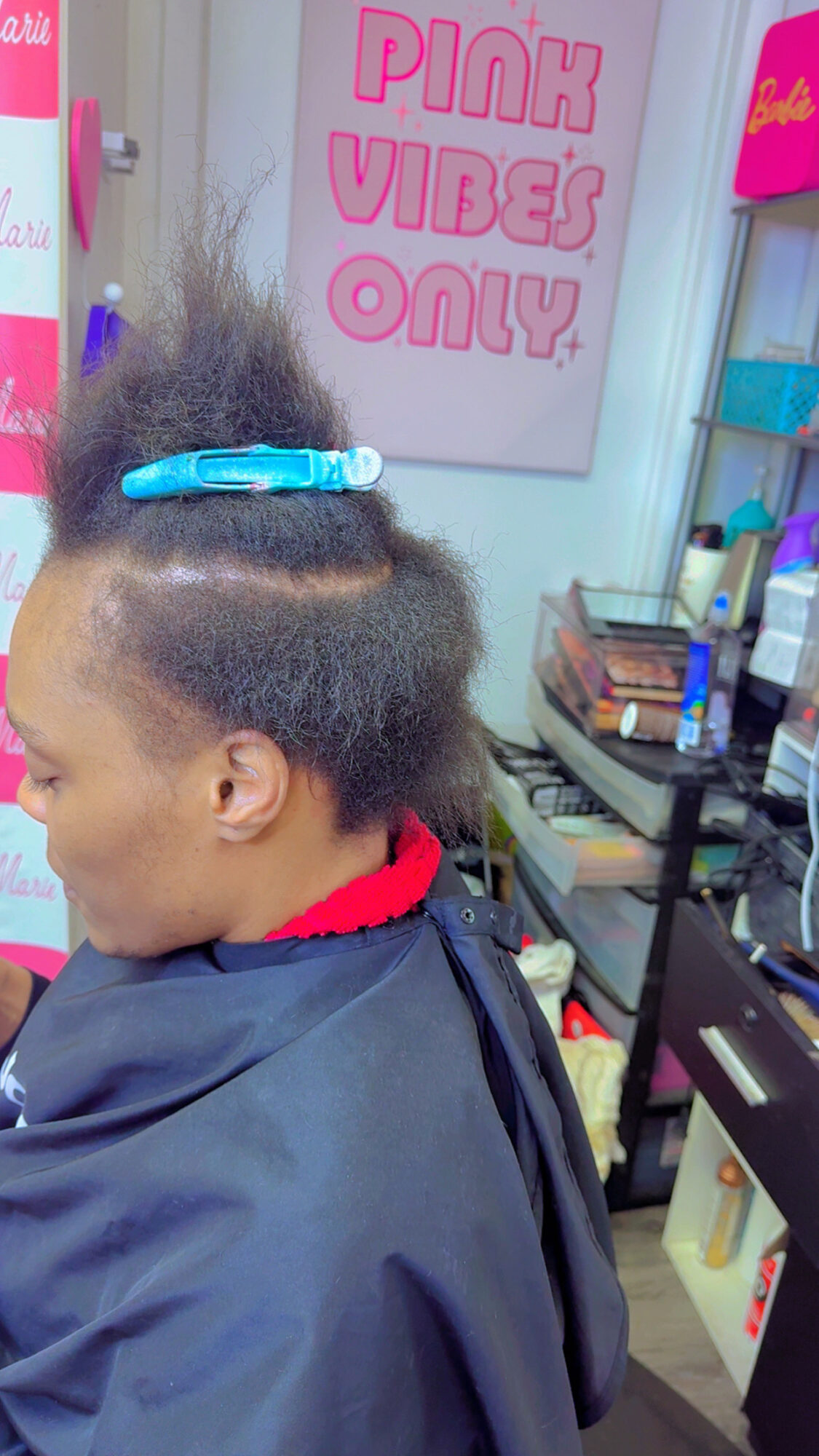 Child with partially styled hair in a salon, wearing a cape, with a sign reading 'Pick Vibes Only' in the background.