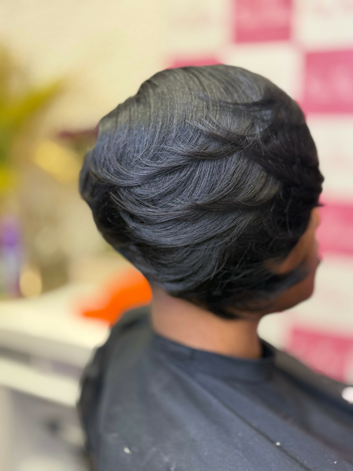 Back view of a woman with a short, styled black hairstyle, sitting in a salon chair.