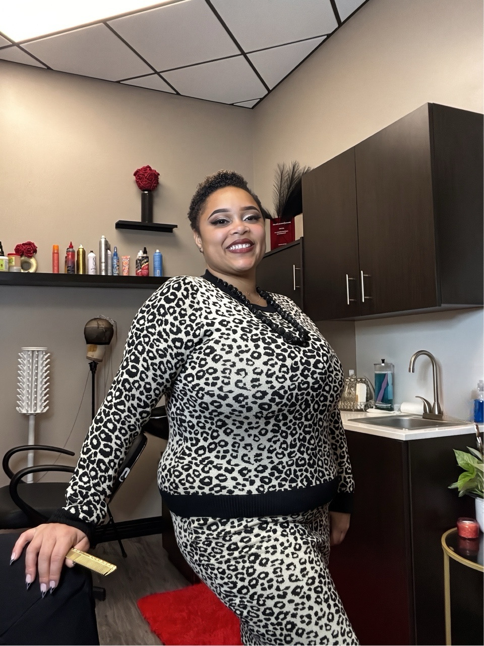 Smiling woman in leopard print outfit standing in a room with cabinets and a sink.