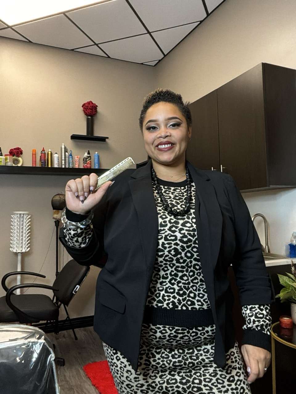 Woman holding a microphone, smiling, in a room with shelves, cabinets, and a chair.