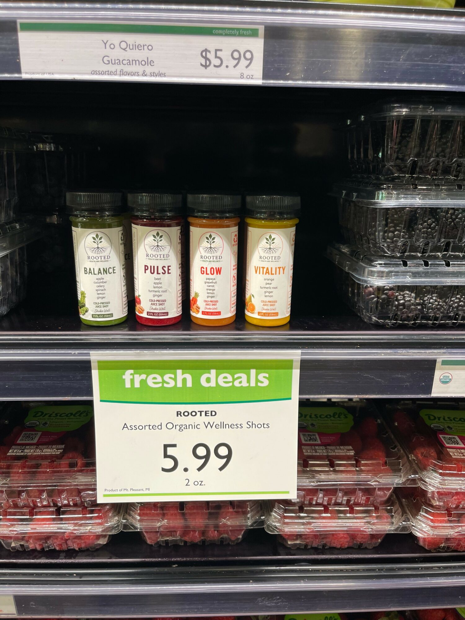Four bottles of juice or flavored water on a store shelf, priced at $5.99, with a green sign indicating fresh deals.