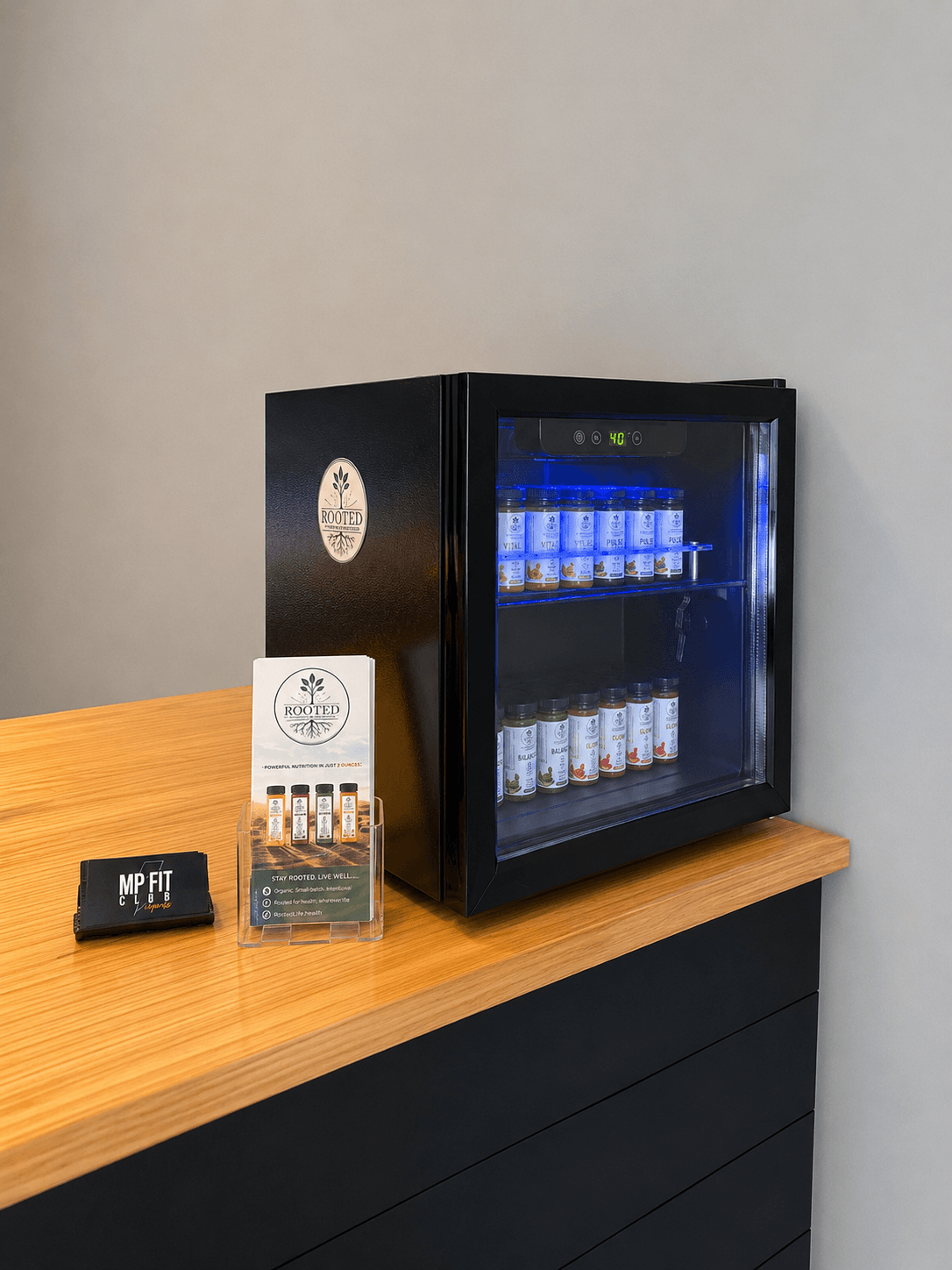 Black mini fridge with glass door displaying beverages, on a wooden table against a plain wall.