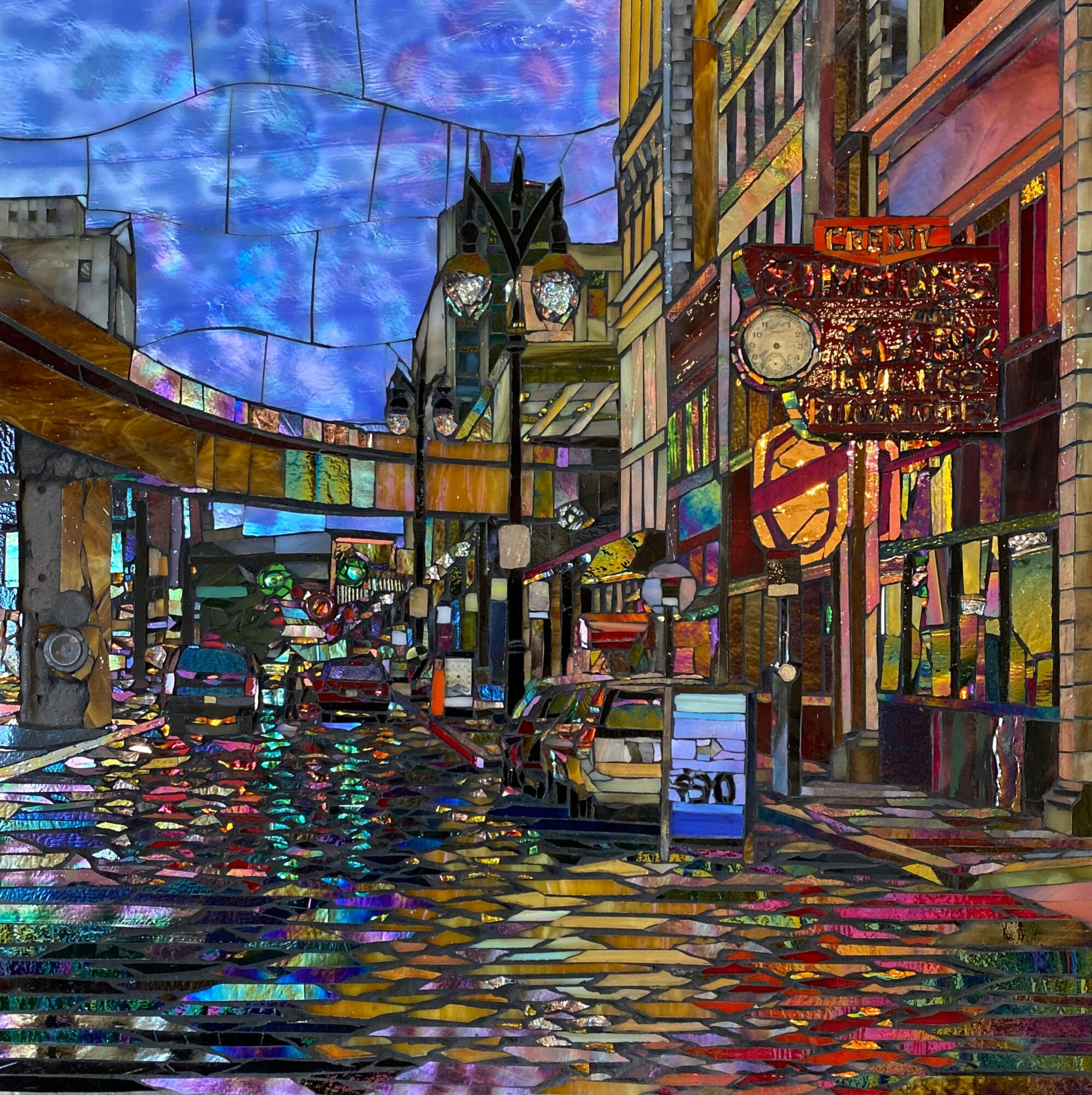 City street scene at night with wet pavement, colorful reflections, buildings, and a clock tower in the background.
