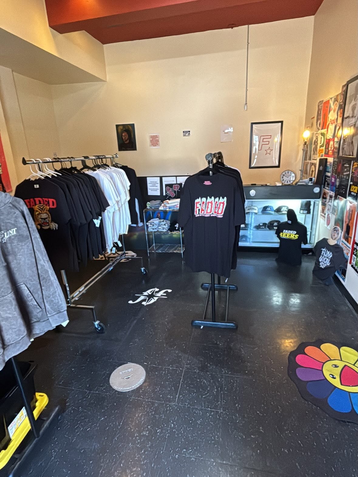 Clothing store with black and white shirts on racks, a mannequin with a black shirt, and colorful wall decorations.