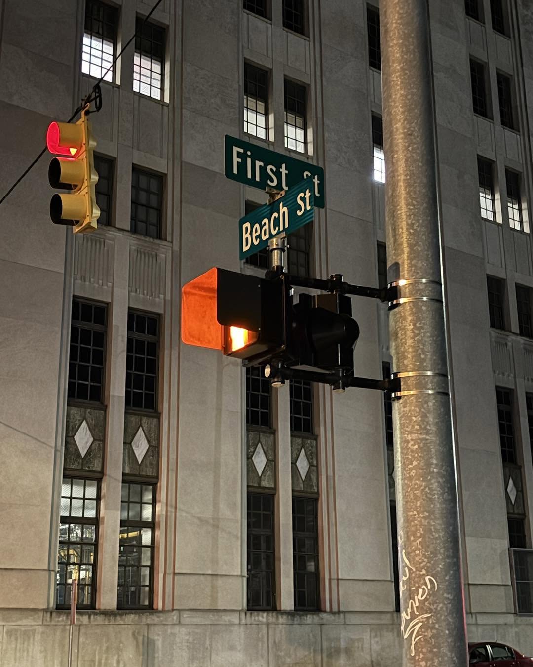 Street sign at intersection of First Beach Street and a traffic light on a tall building background.