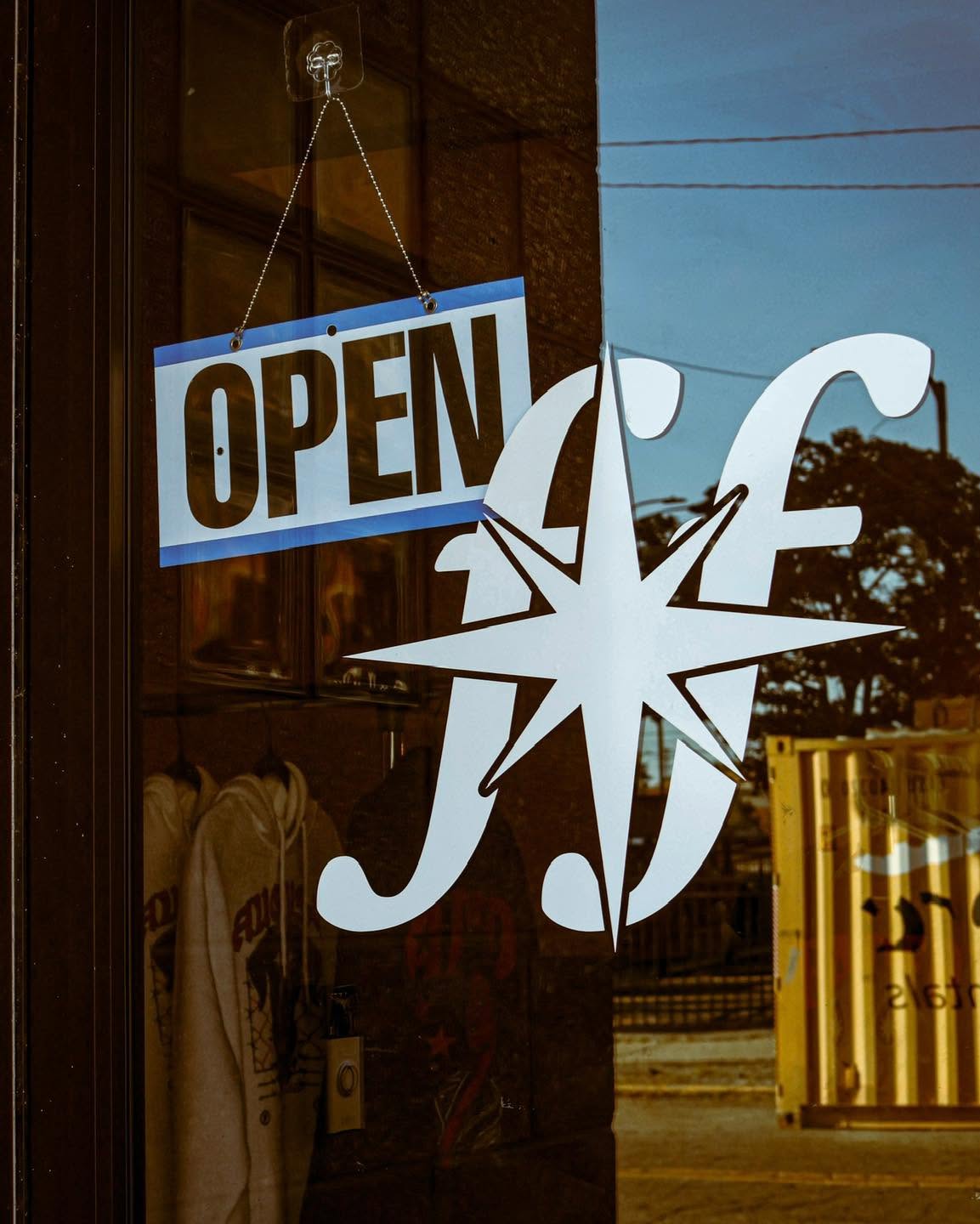 Store window with an open sign and a decorative star-shaped ornament, outside view with trees and a yellow container.