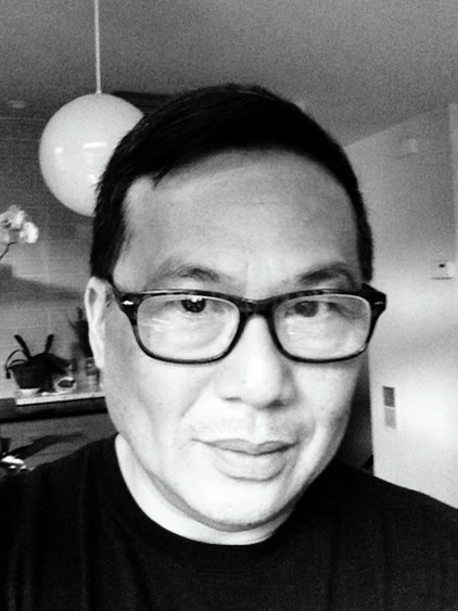 Portrait of a person with short dark hair, glasses, and a slight smile, indoors with a hanging light fixture in the background.