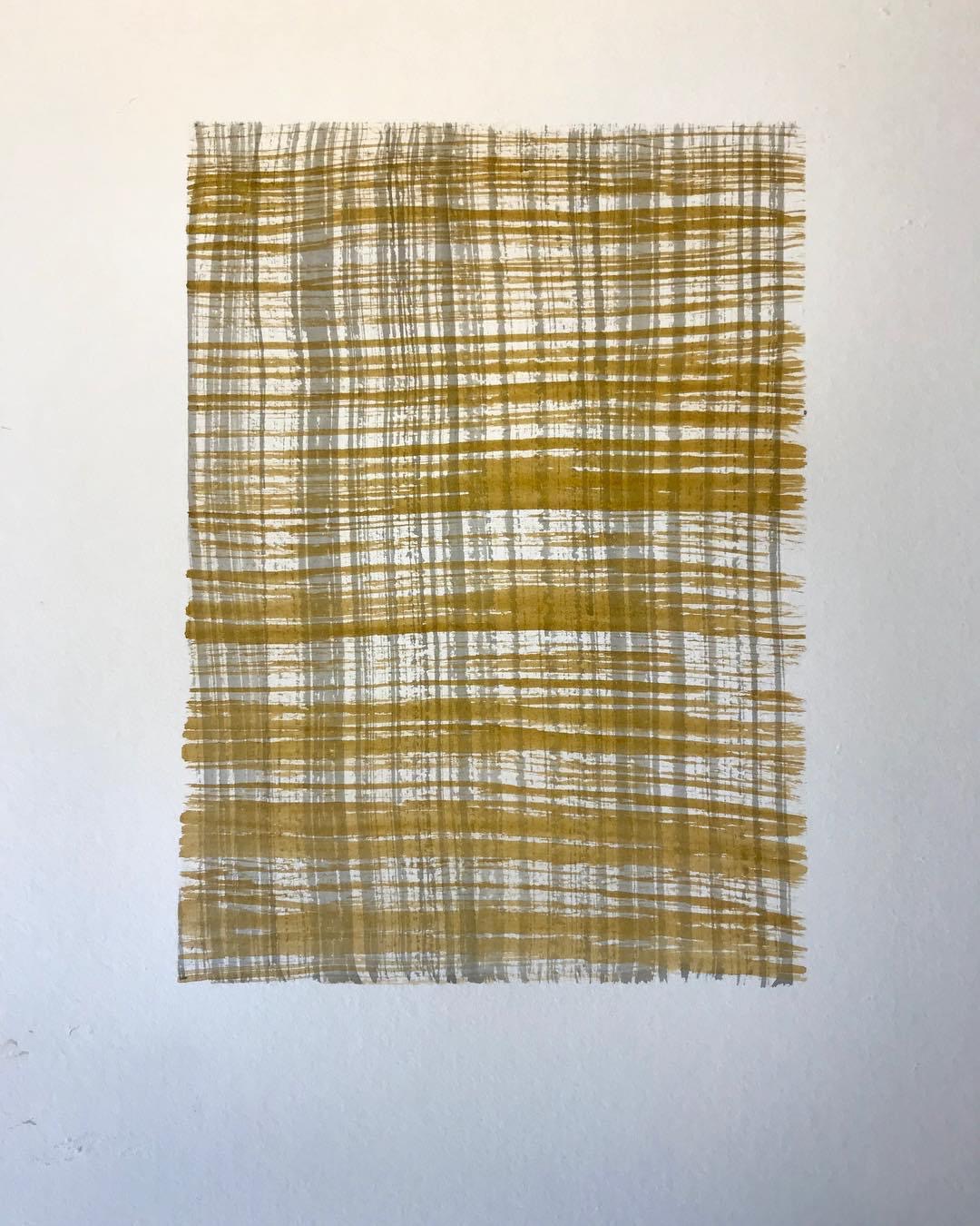 A rectangular woven textile with a yellow and white checkered pattern hanging on a white wall.