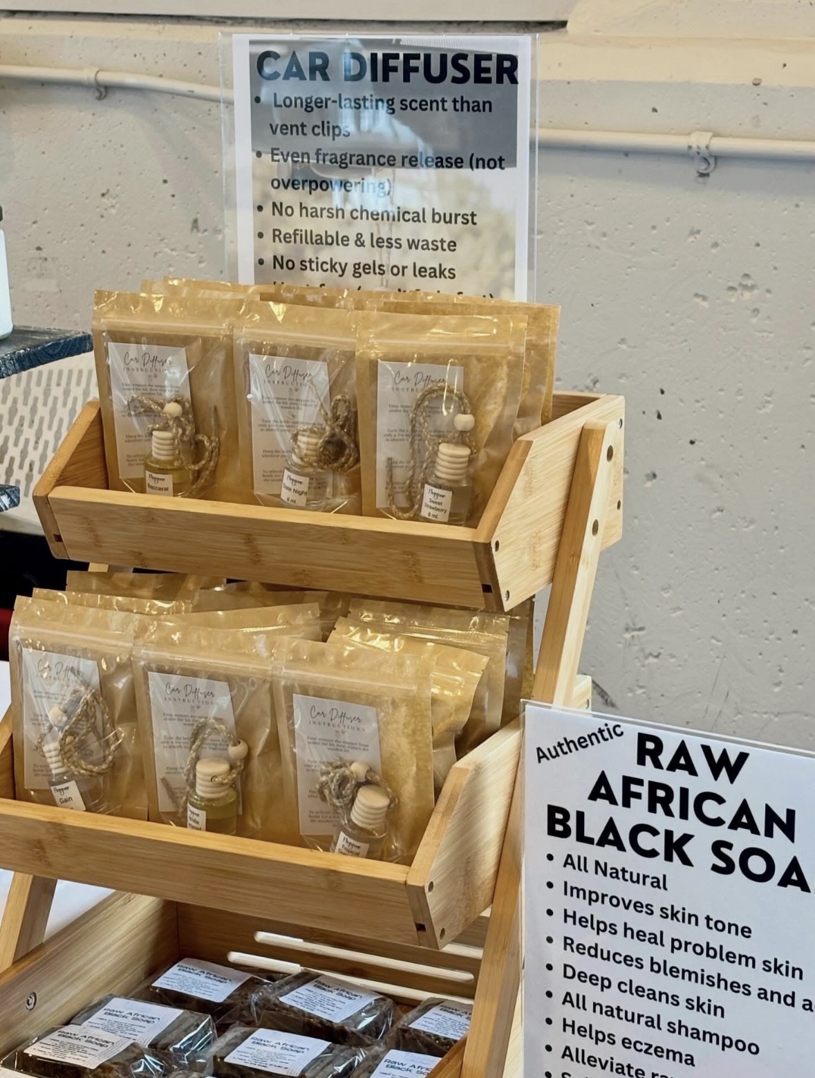 Wooden display stand with black soap products and informational signs, against a white wall background.