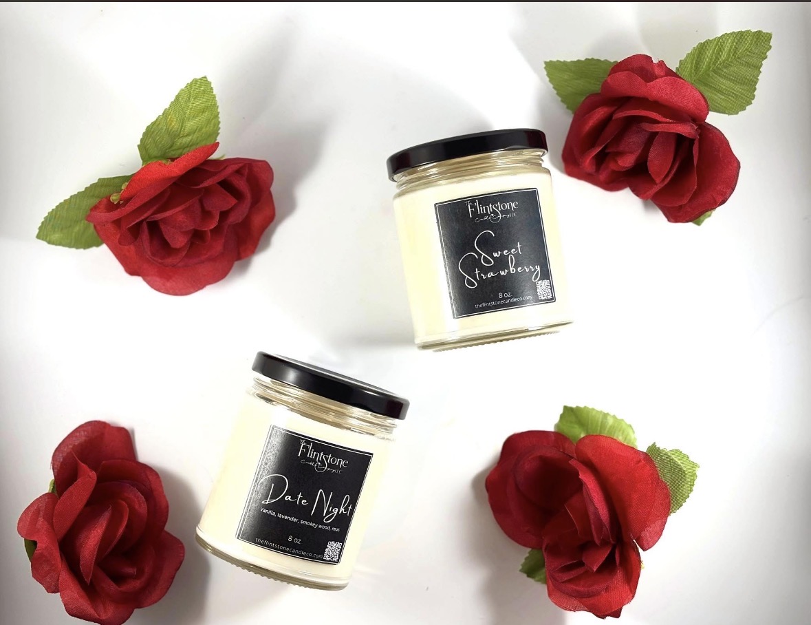Two candles with black labels and four red roses with green leaves on a white background.
