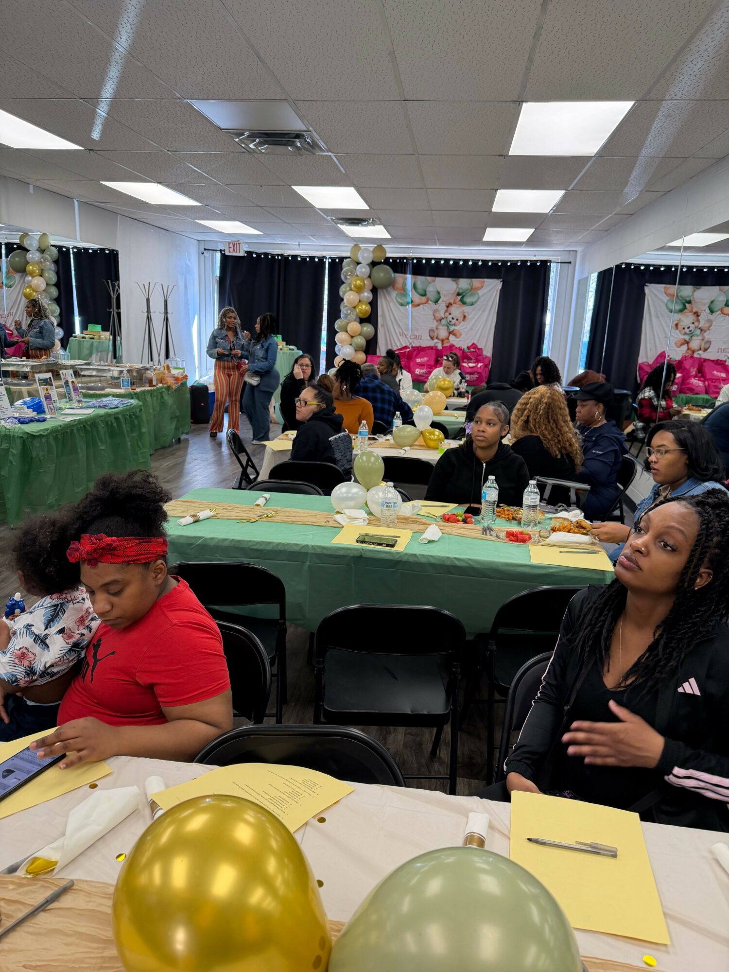 People gathered around a table with balloons and decorations, celebrating indoors with a cake and party supplies.