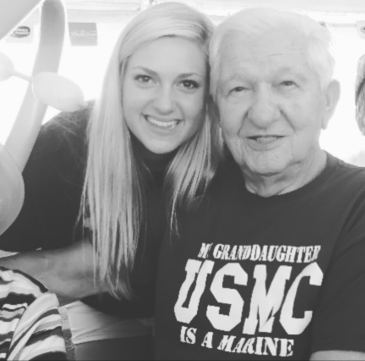 A young woman and an elderly man smiling together, the man wearing a T-shirt with text about a Marine, in black and white.