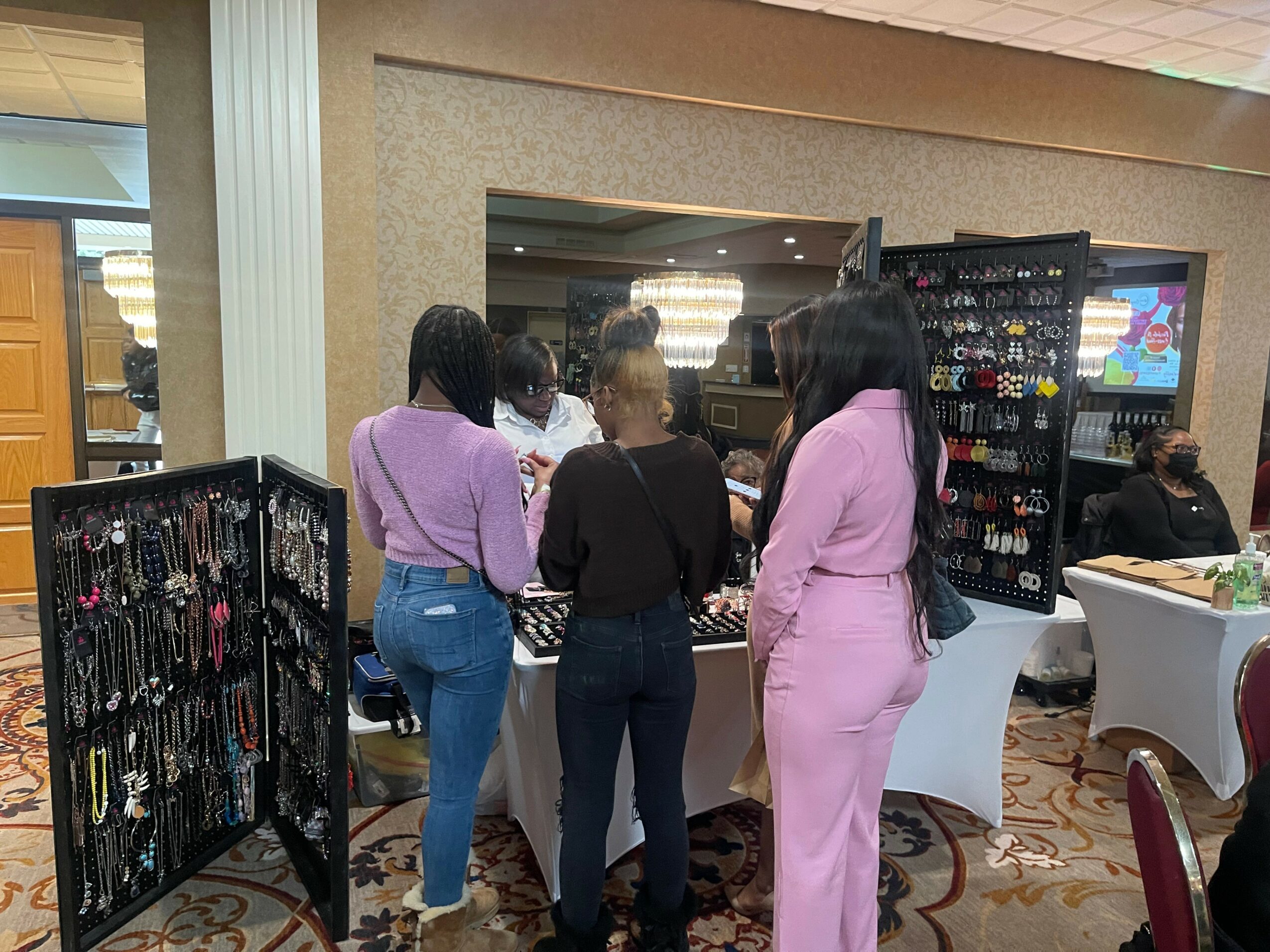 Group of people gathered around a table in an indoor setting, with display racks of jewelry nearby.