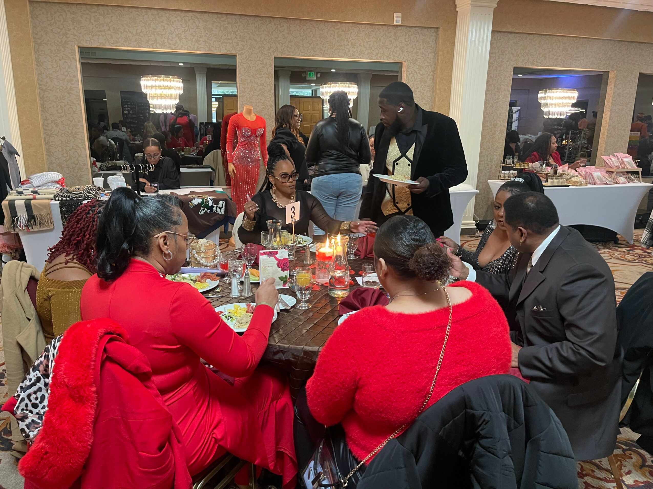 Group of people seated around a table at a social event, with others standing and talking in the background.