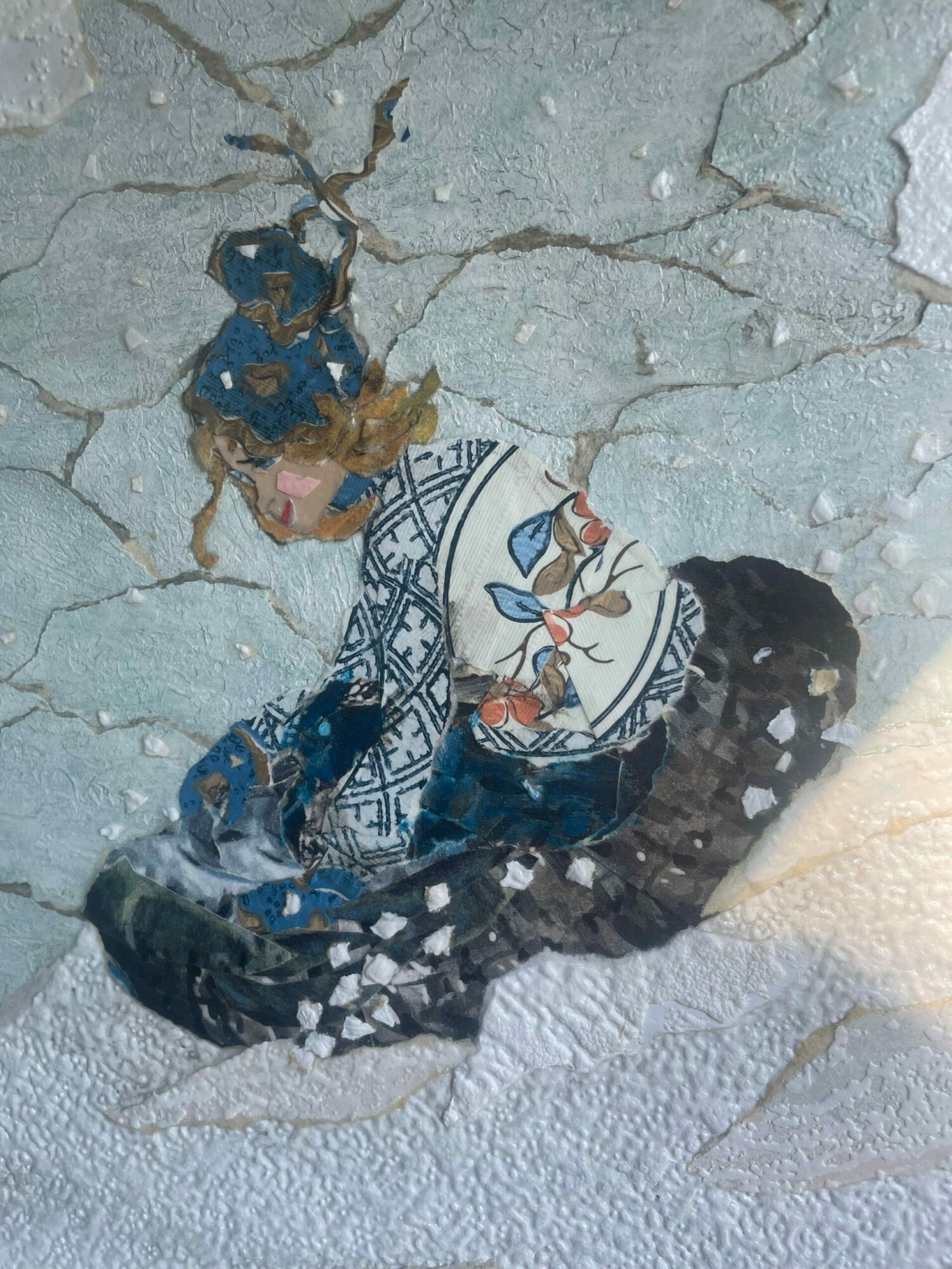 A person wearing a patterned blue and white garment lying on a cracked, textured surface.