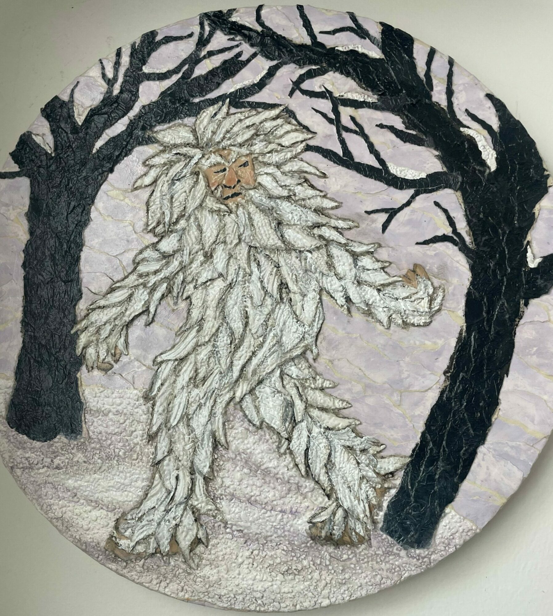 Embroidery of a white cat with a bushy tail, lying among dark tree branches, on a circular fabric background.