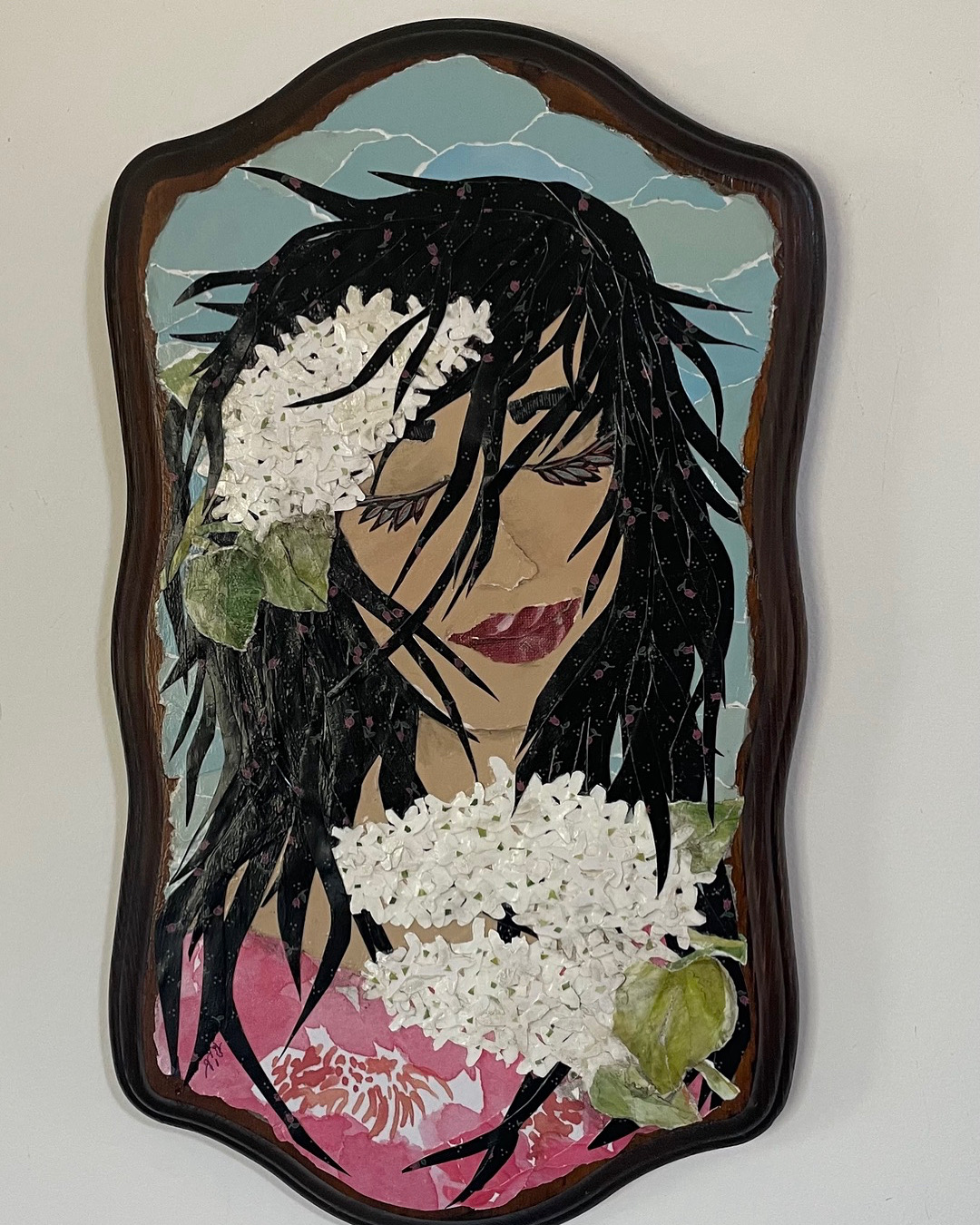 Mirror with a painted portrait of a woman with black hair, red lips, surrounded by white flowers, and a cloudy sky background.