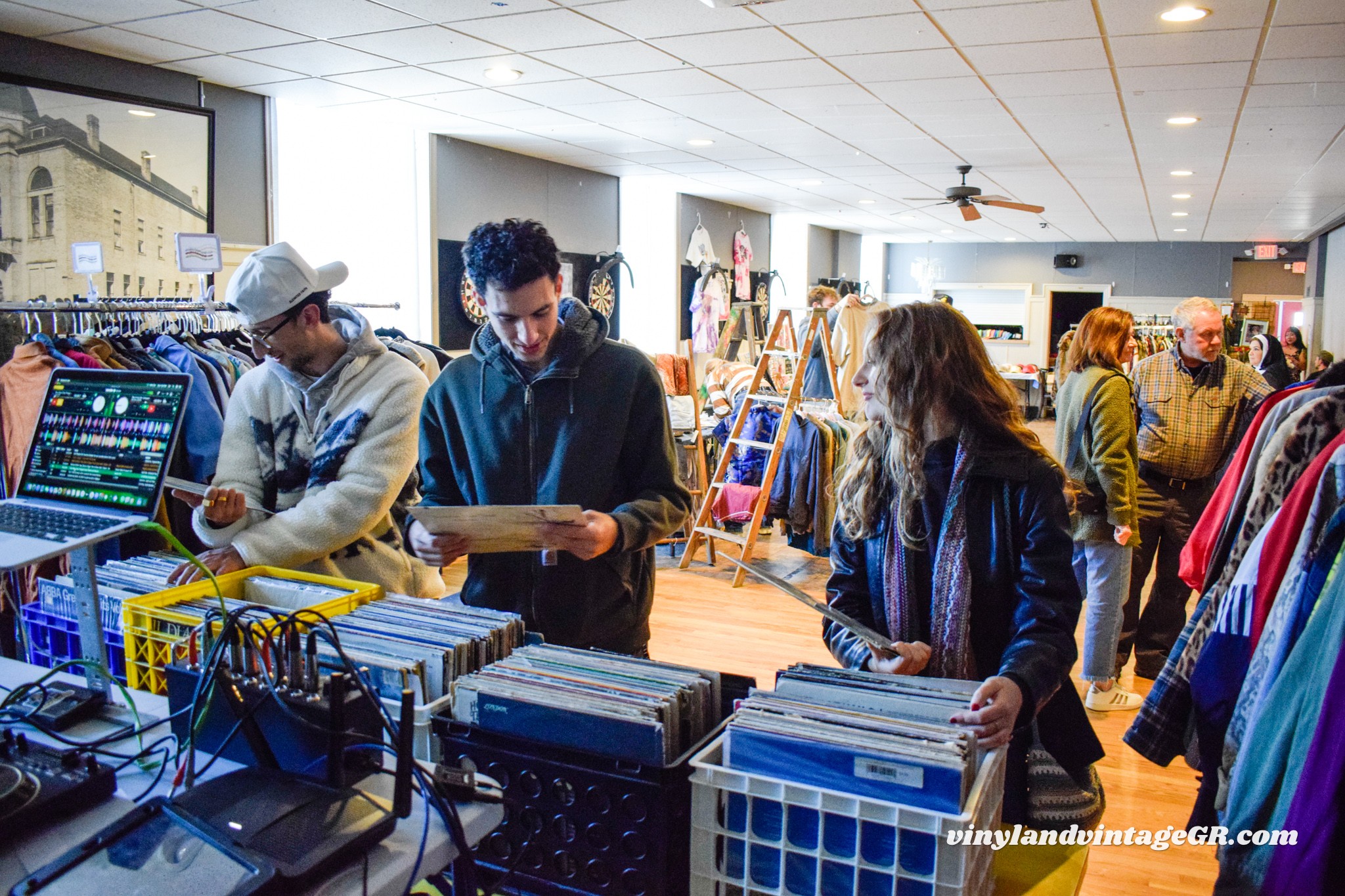 People shopping at a clothing store, browsing racks and using electronic devices inside the store.