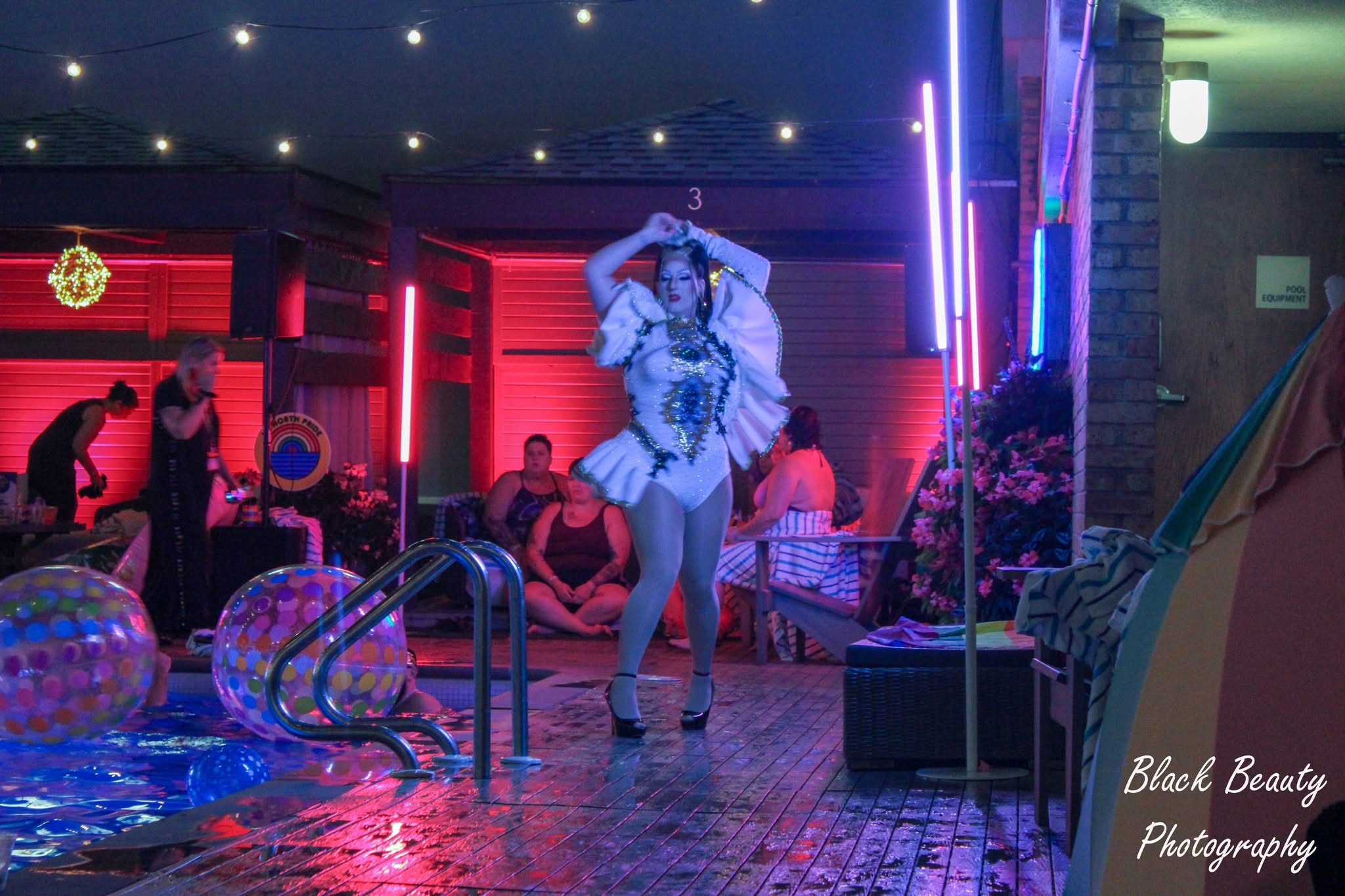 Person performing on stage with colorful lights and audience in background, party setting with decorations and seating area.
