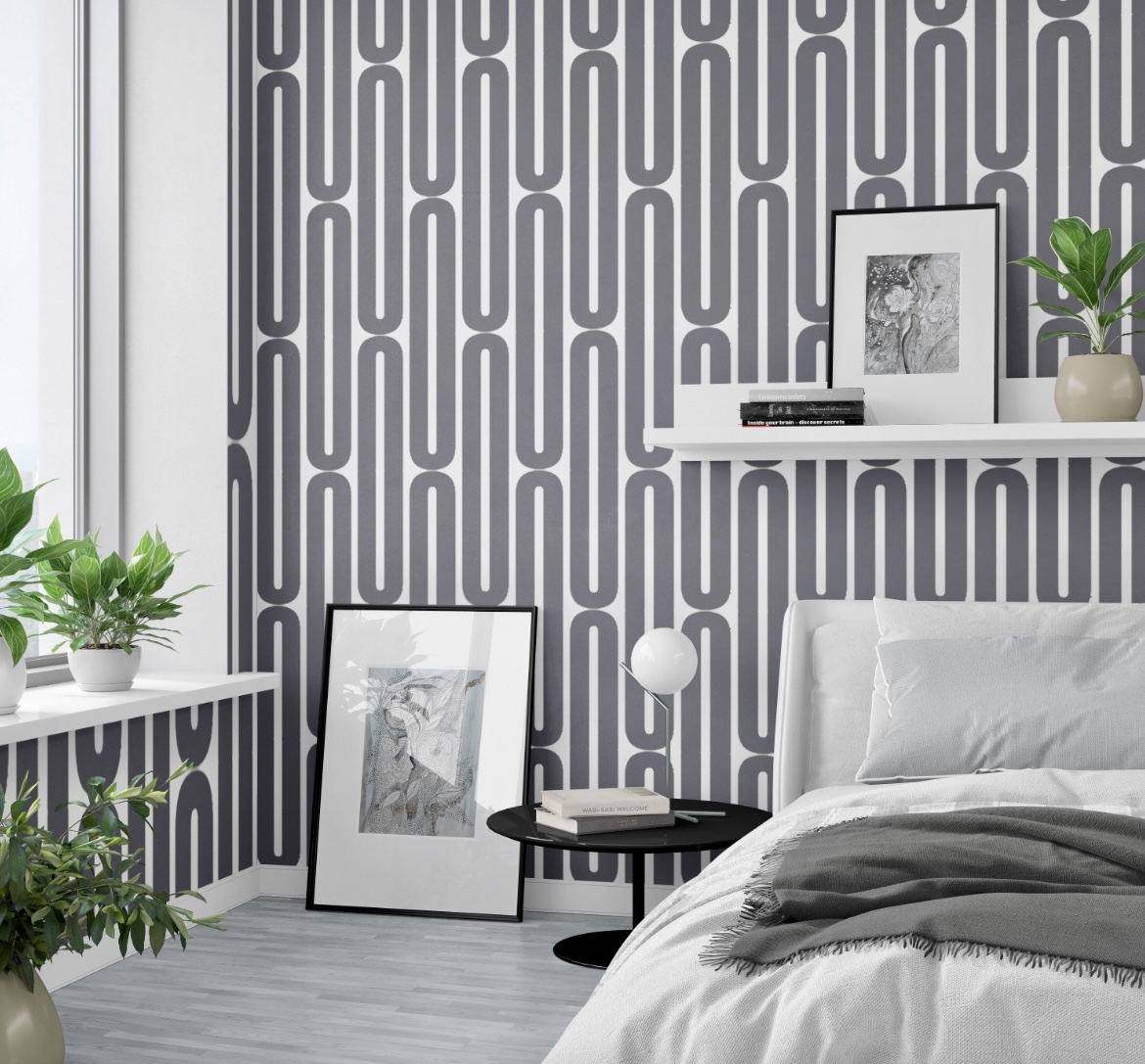 Bedroom with patterned wallpaper, white bed, floating shelf with framed picture and plant, and a side table with a lamp.