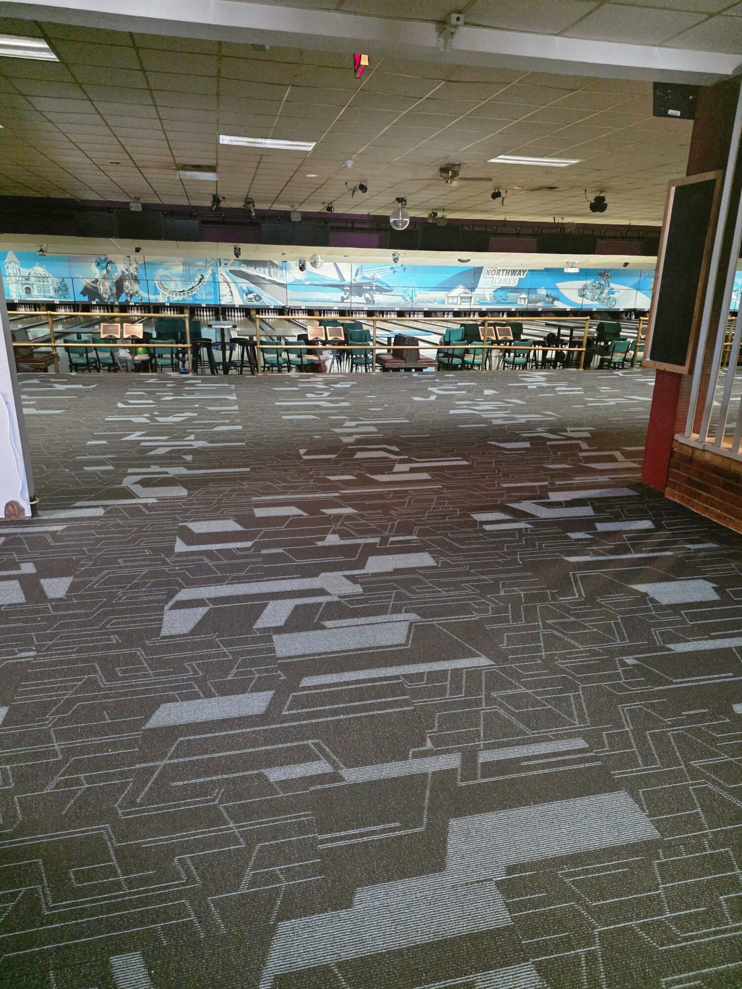 Empty indoor space with patterned carpet, large windows, and a view of a swimming pool area outside.