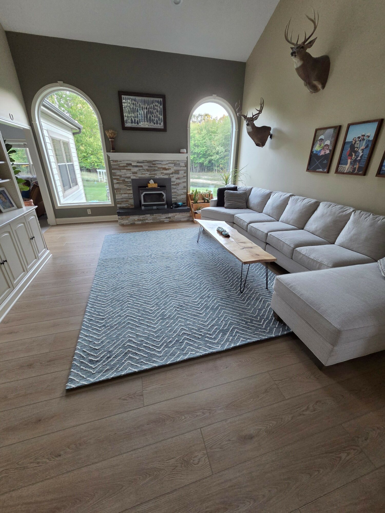 Living room with a white sofa, a blue rug, a fireplace, and large windows showing greenery outside.