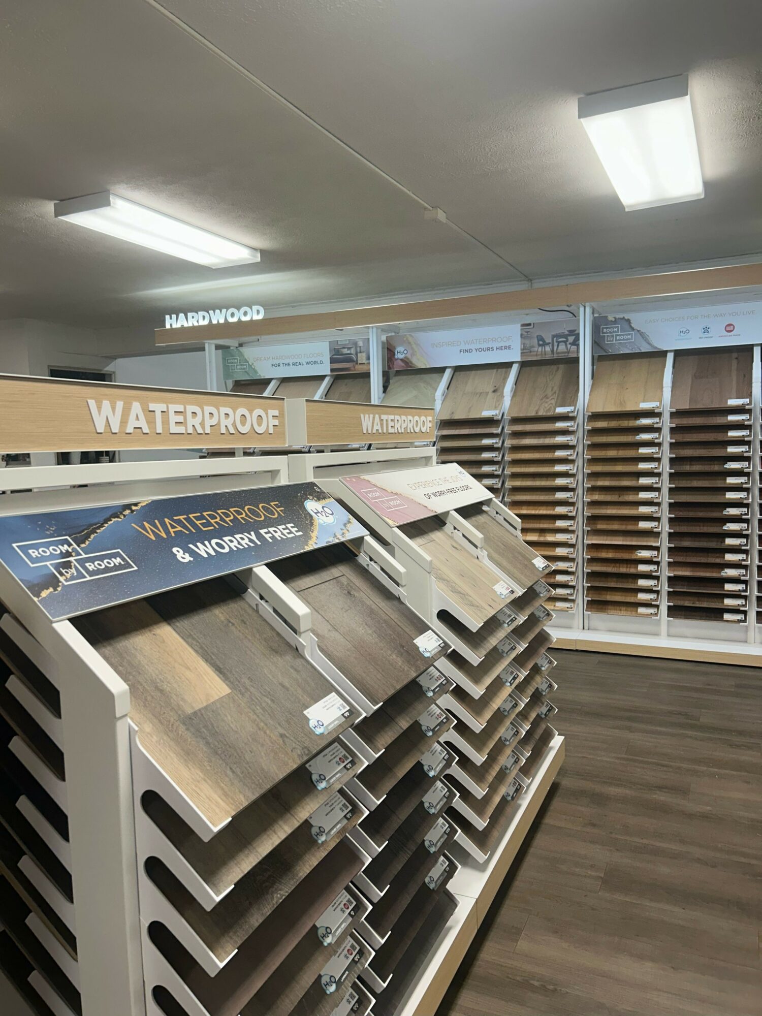 Display of wood flooring samples in a store, arranged on angled racks with labels, viewed from the side.