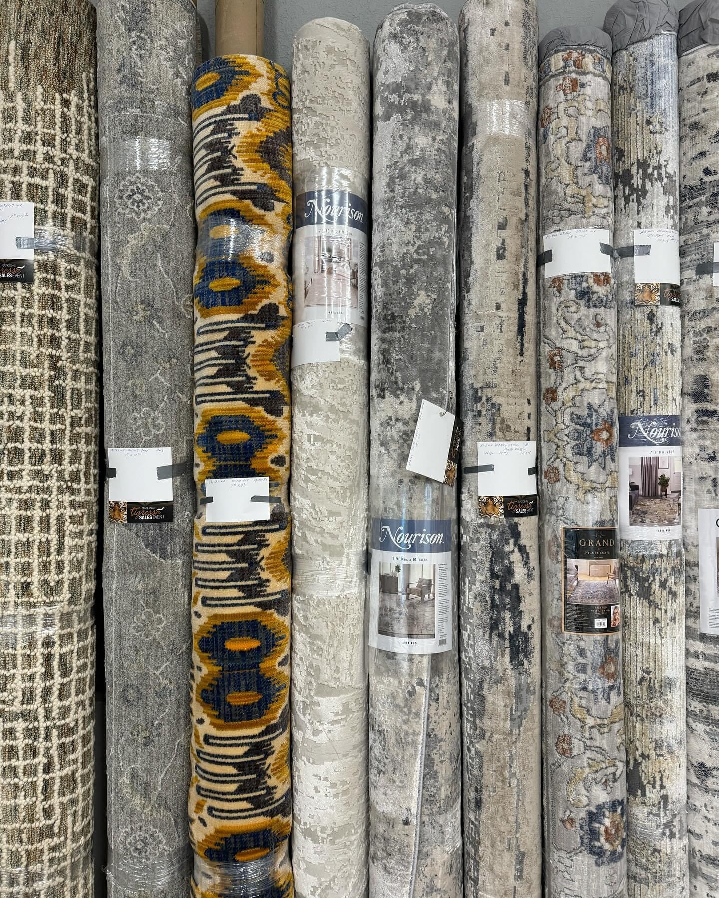 Upright display of rolled wallpaper with various patterns and colors, some with tags attached.