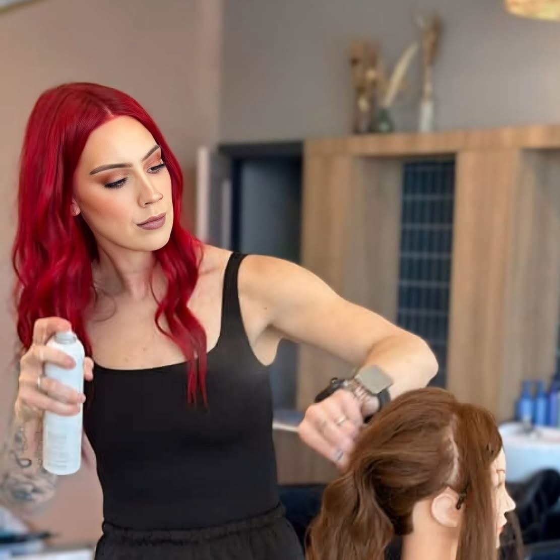Woman with red hair sprays hair of a person with brown hair in a salon. Modern interior background.