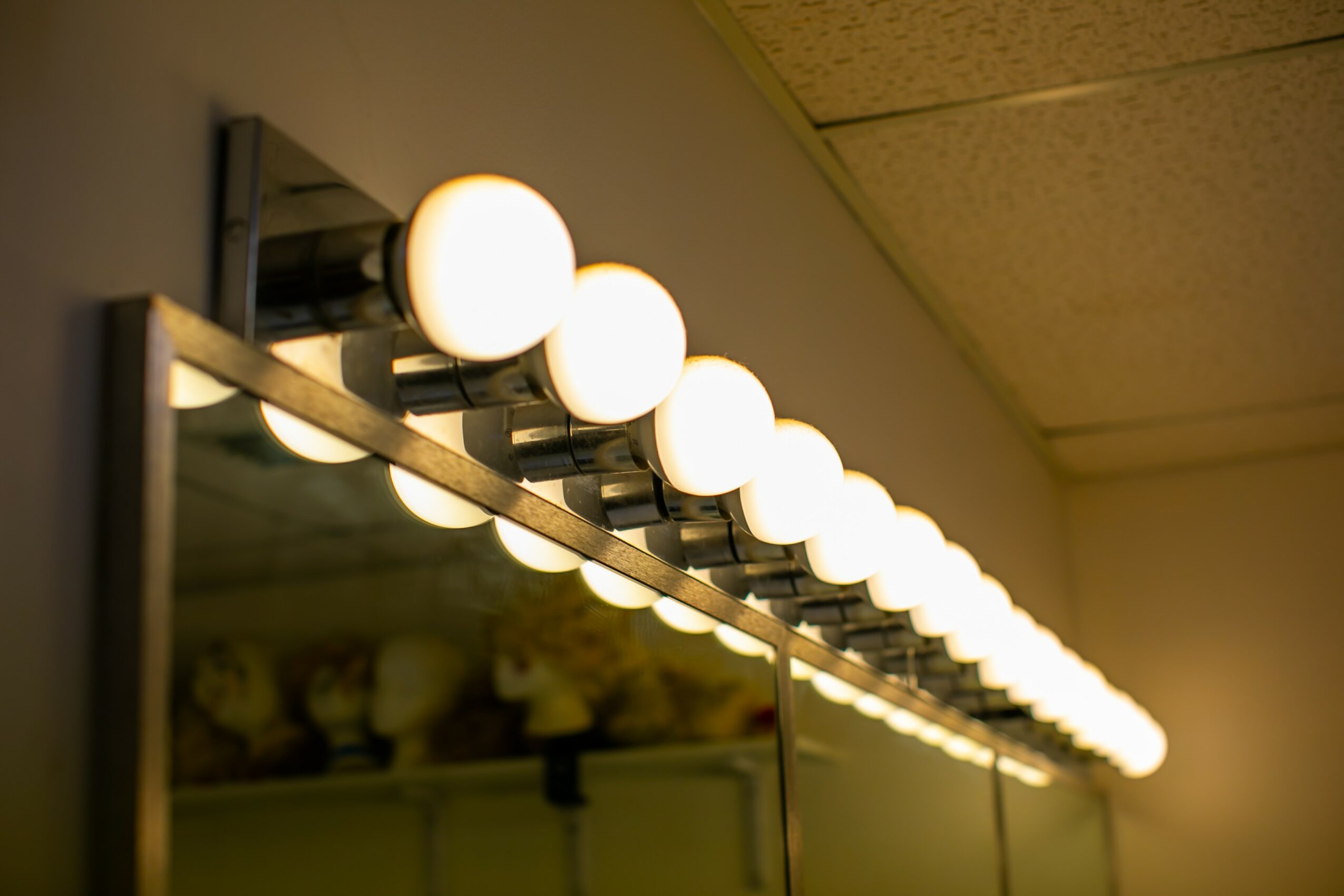 Row of bright round lights mounted on a wall above a mirror, illuminating a room.