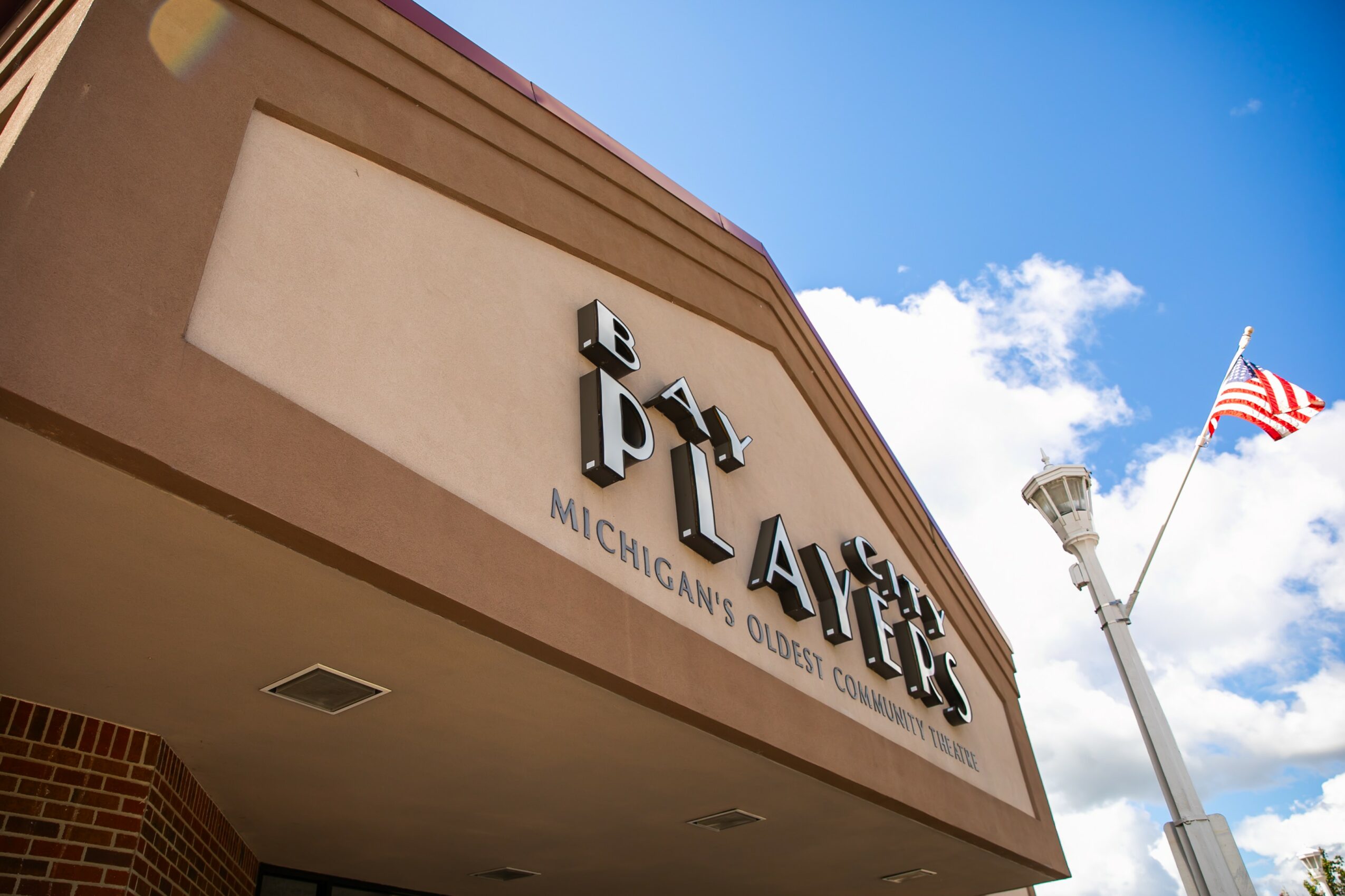 Sign for Playhouse Michigan's oldest theater, with a blue sky and American flag in background.