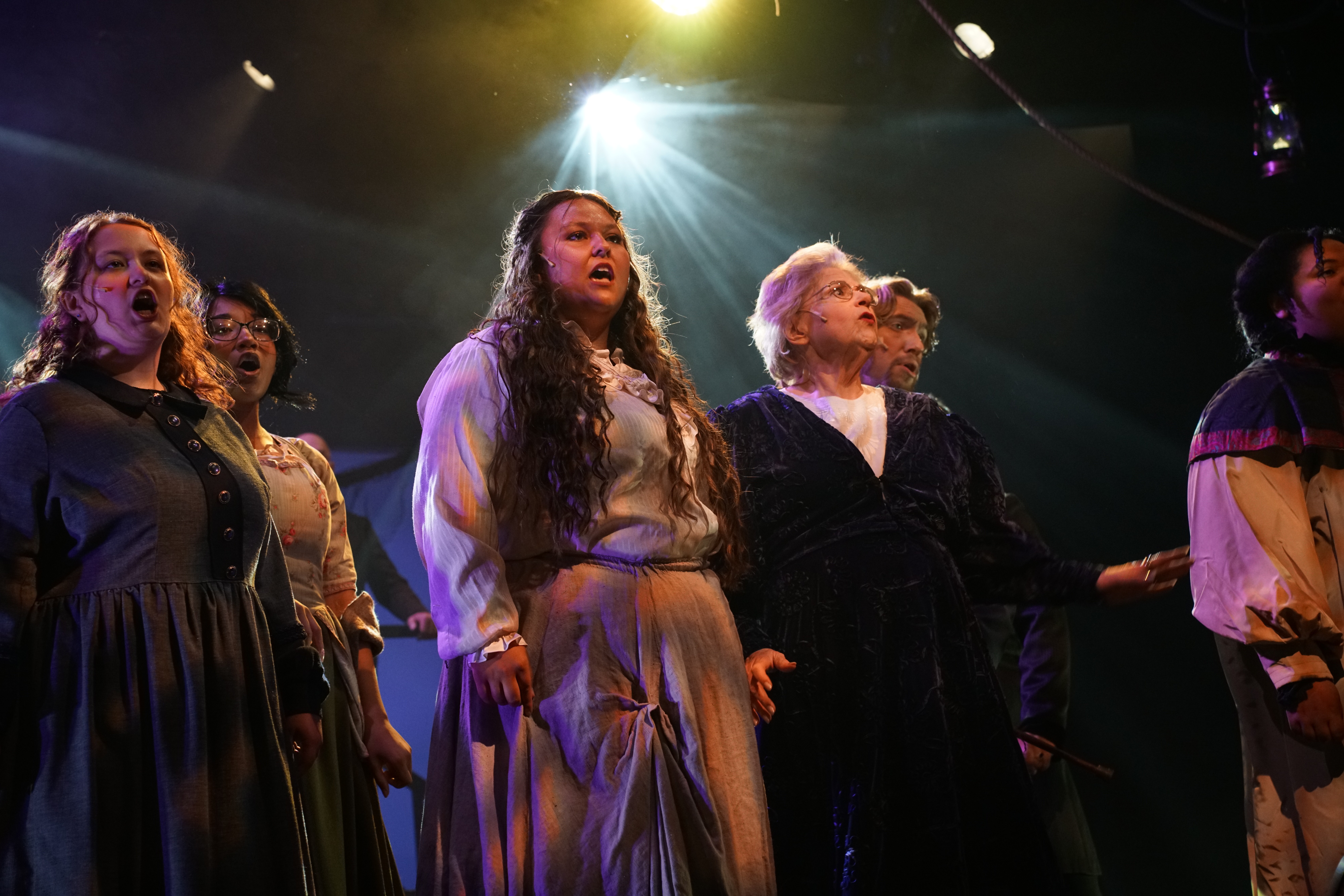 Group of women singing on stage under bright lights, with focused expressions, in a performance setting.