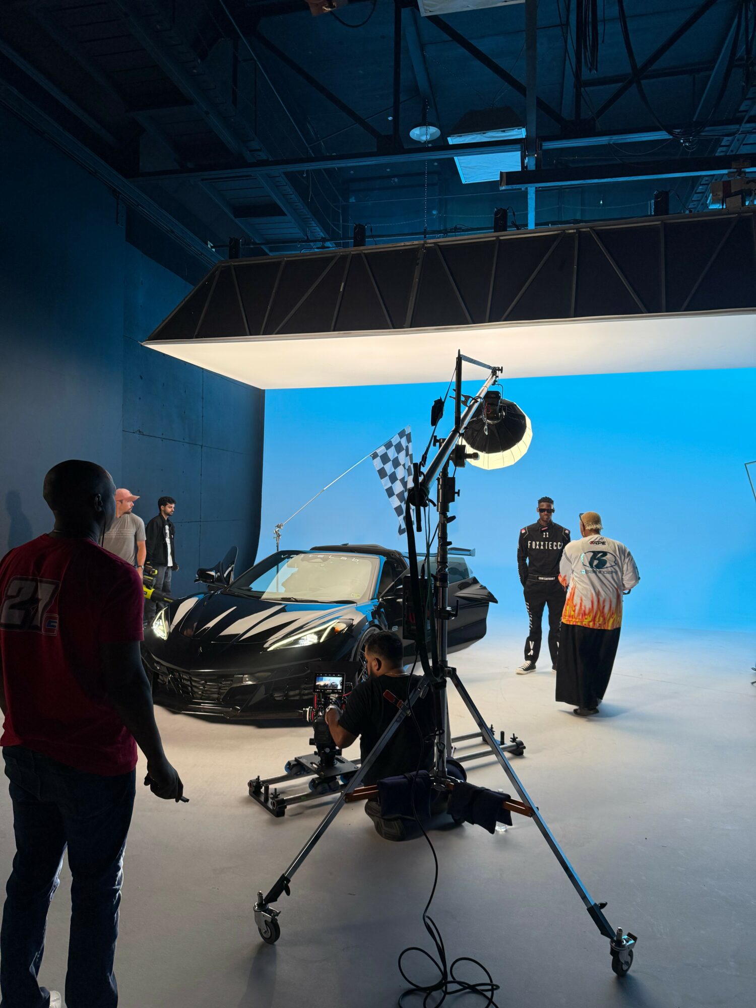 Studio with a black sports car, people, and a blue background, filming equipment in foreground.