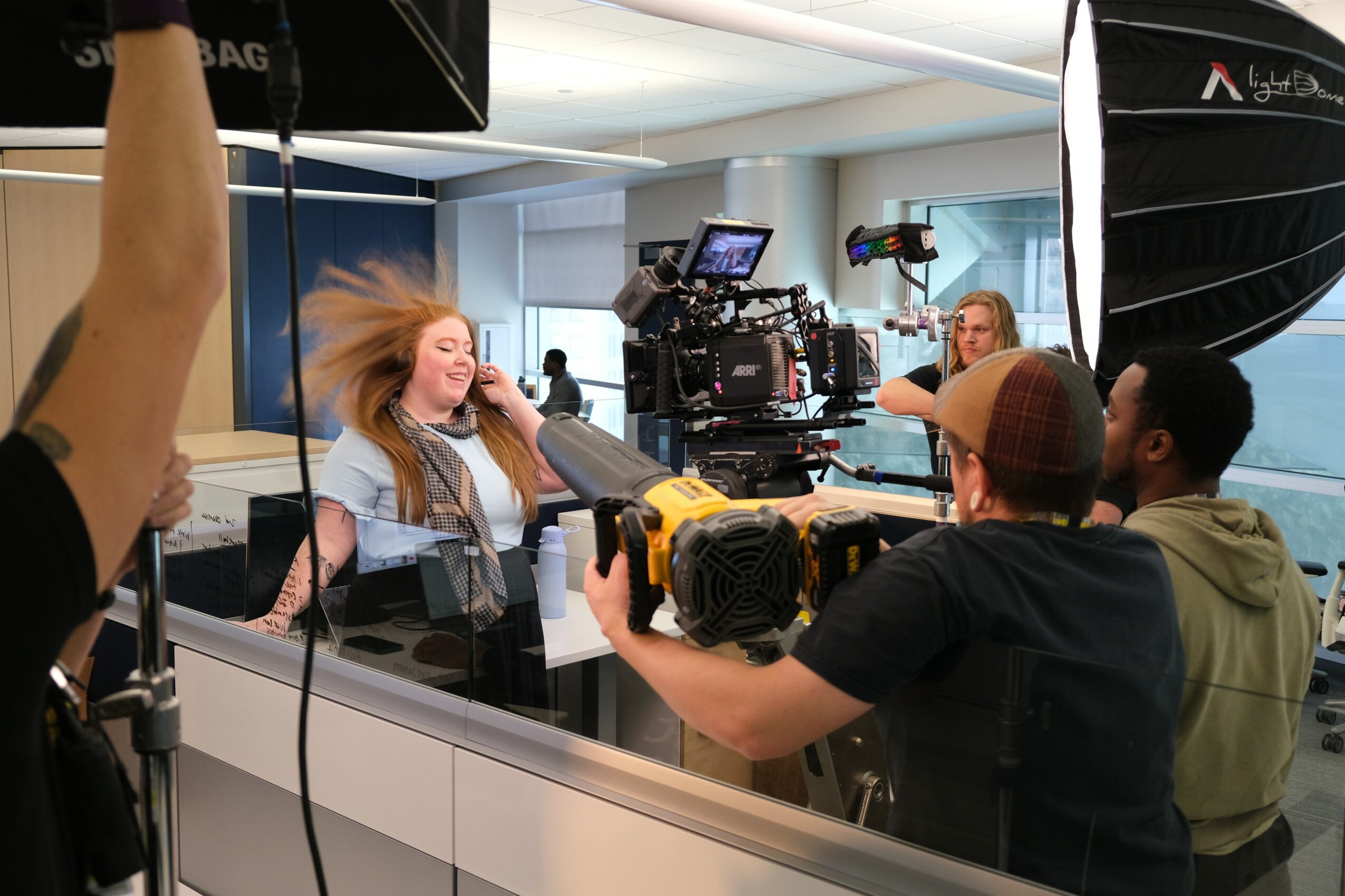 A woman with long hair is being filmed in a studio, surrounded by camera equipment and crew members.