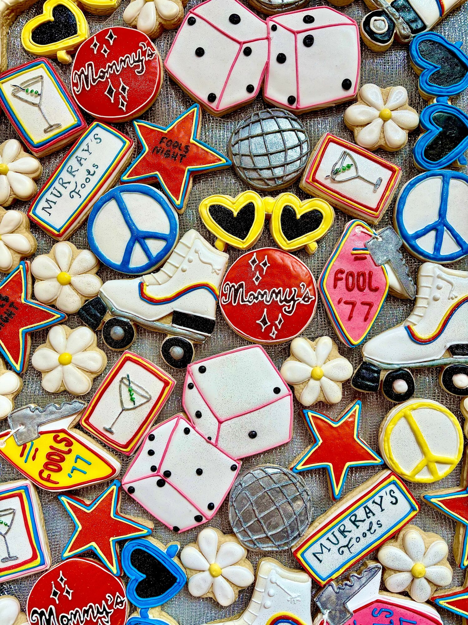 Colorful assortment of candies and cookies with peace signs, hearts, dice, flowers, and labels, arranged in a pattern.