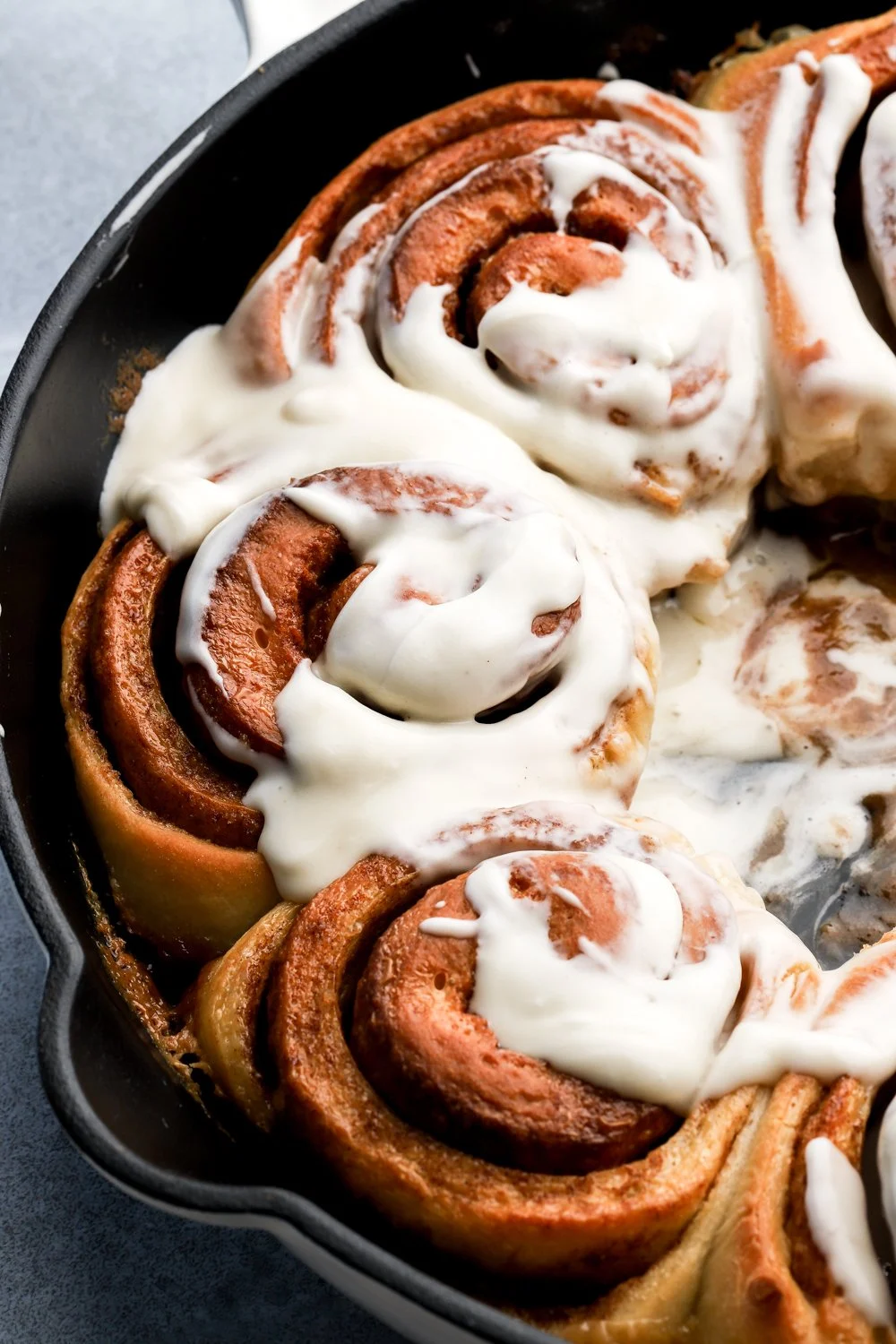 Cinnamon rolls with white icing in a black baking dish, viewed from above.